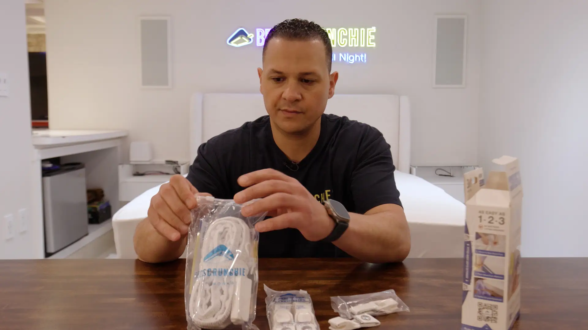 Jack Nekhala is sitting at a desk while taking his bed scrunchie product outside of its package.