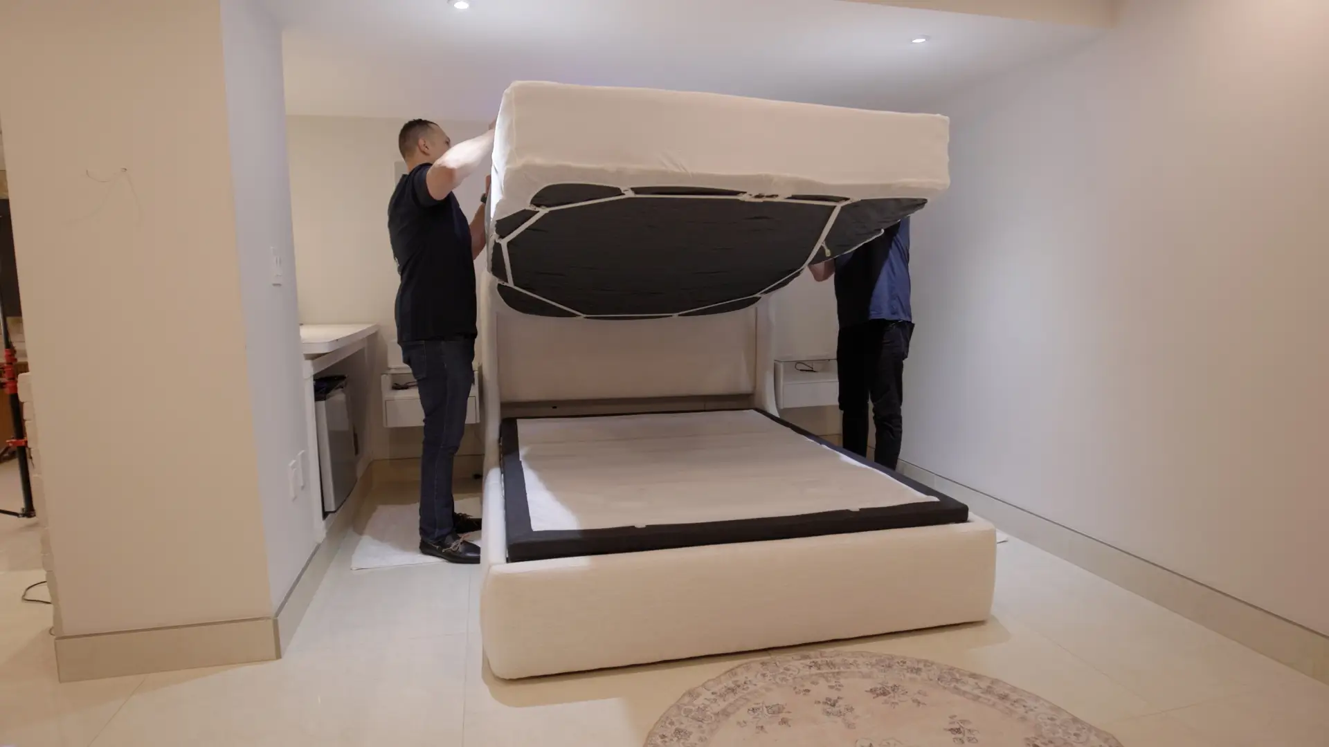 Two men holding up a mattress, revealing the bed scrunchie design that secures sheets and mattress toppers.