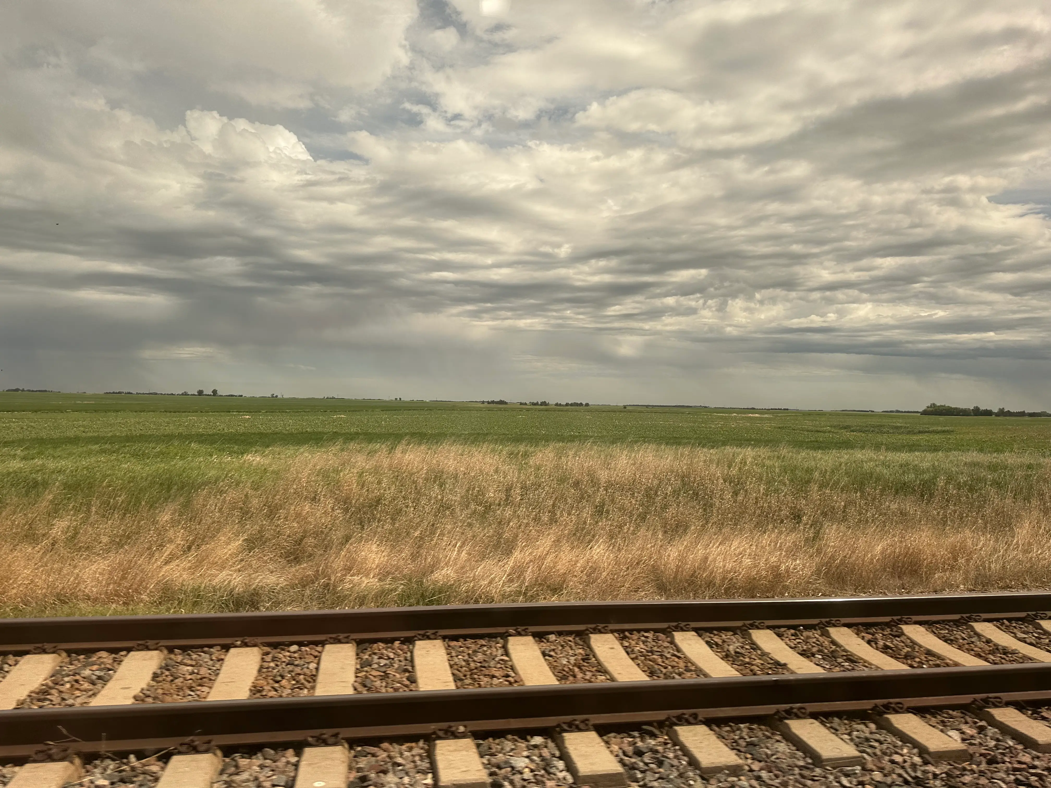 Railroad tracks run past open grassland beneath a cloudy sky.