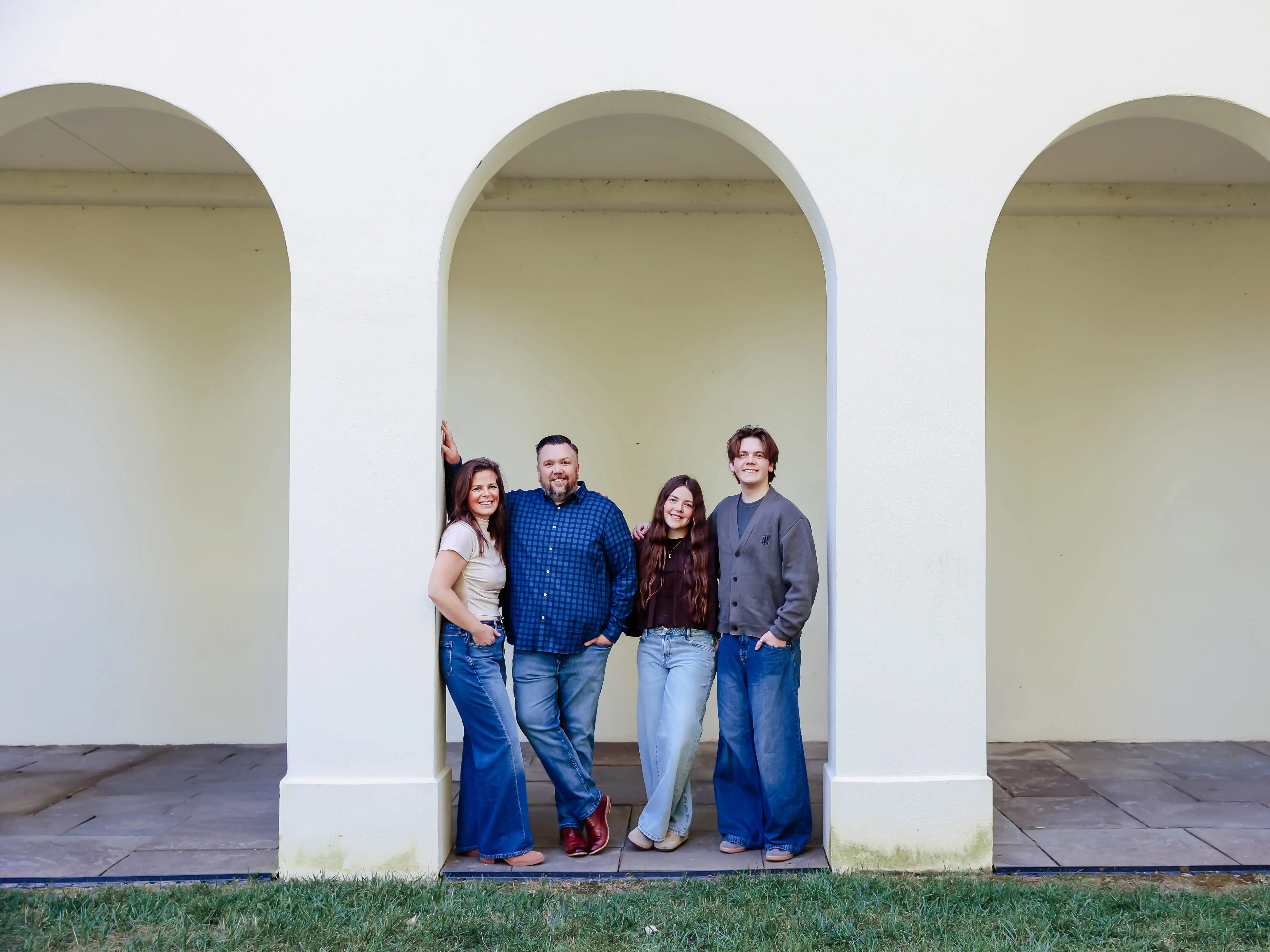 Four people pose together beneath a white arched colonnade with grass in the foreground.