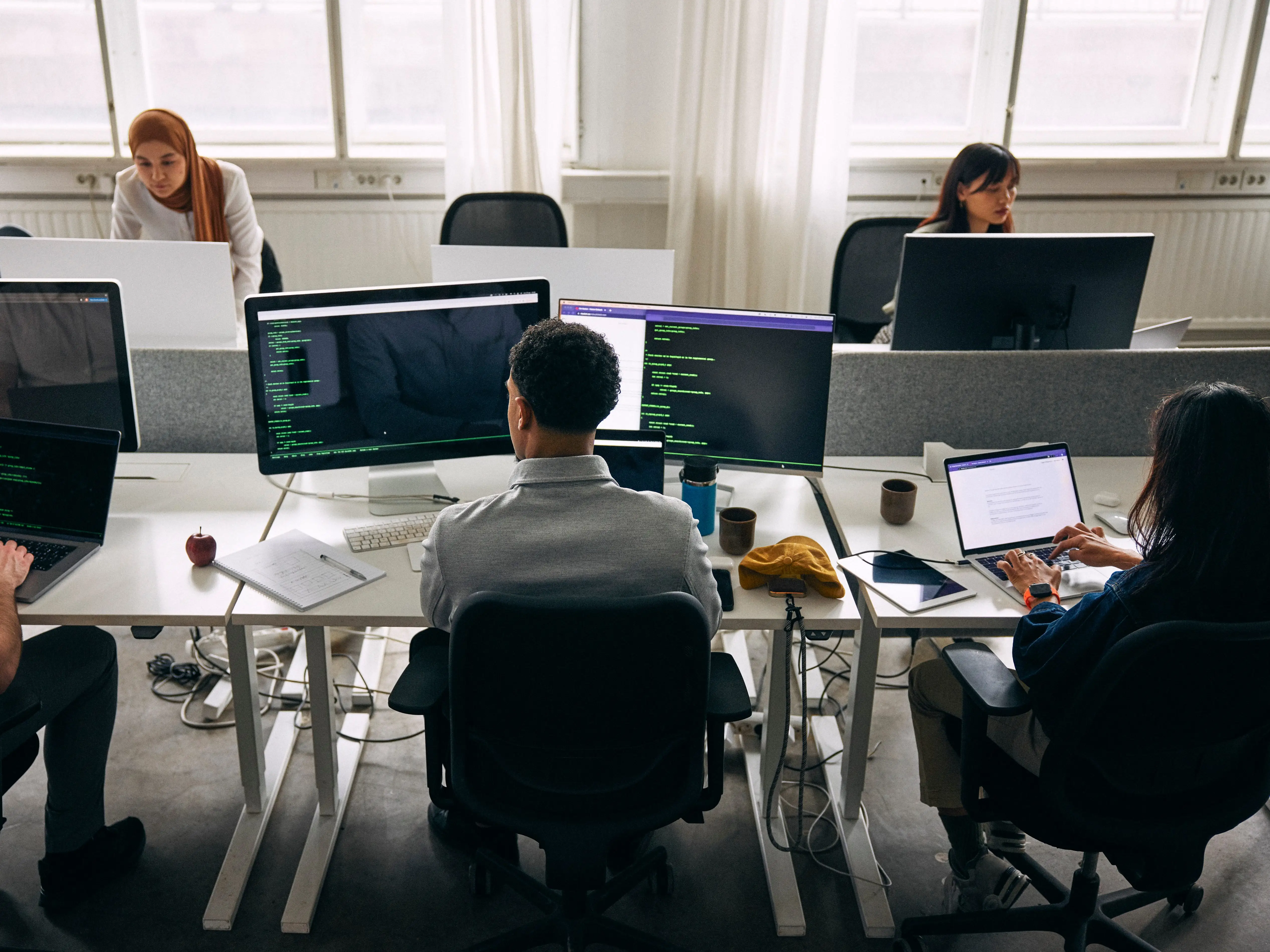 Multiple people work with computers with code-filled monitors in an office.