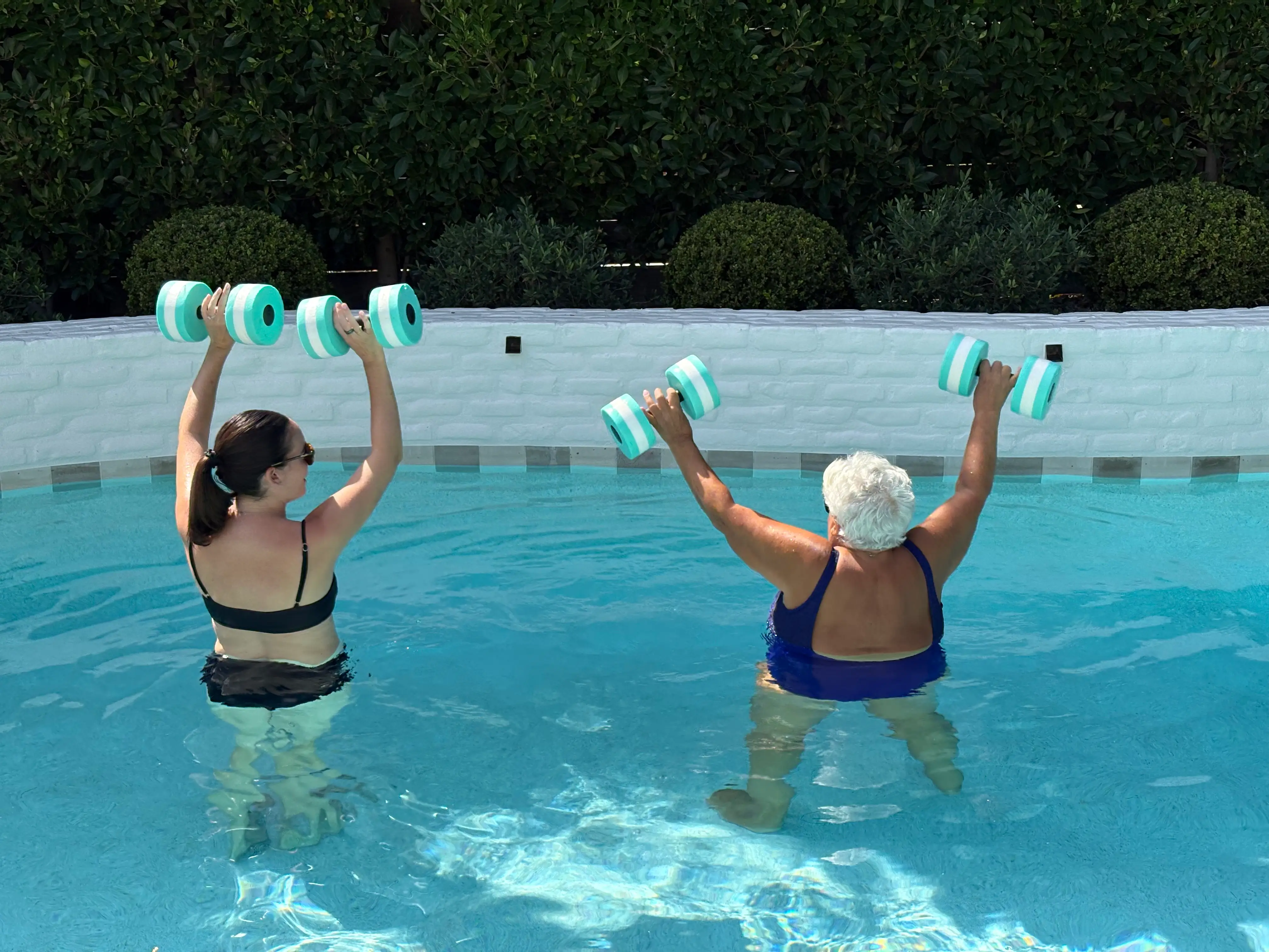 Blake and her grandmother face away from the camera while lifting weights above their heads in the pool.