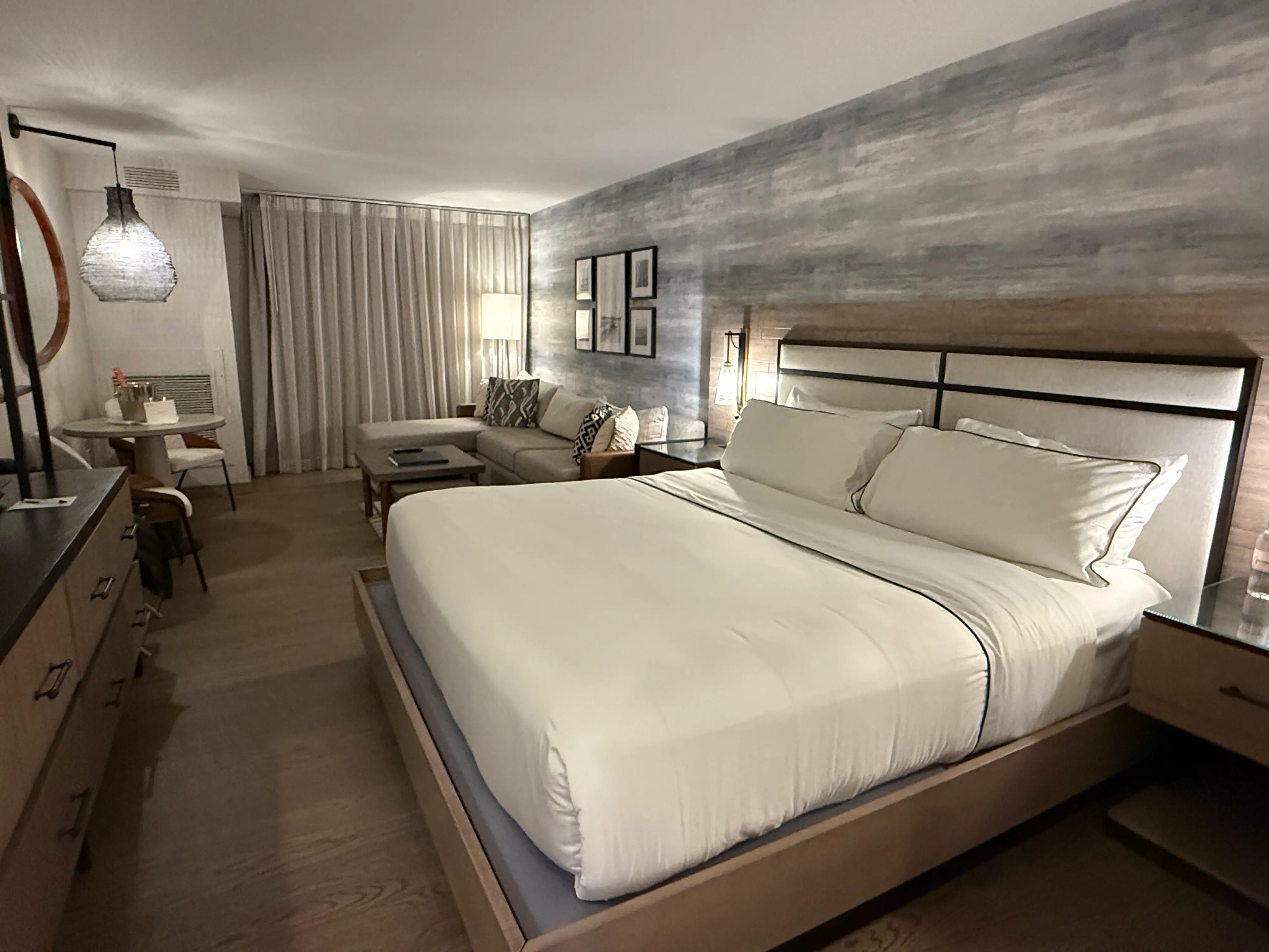 A hotel room at Gurney's in Montauk has a large bed, seating area, desk, lamps, curtains, and wood-toned decor.