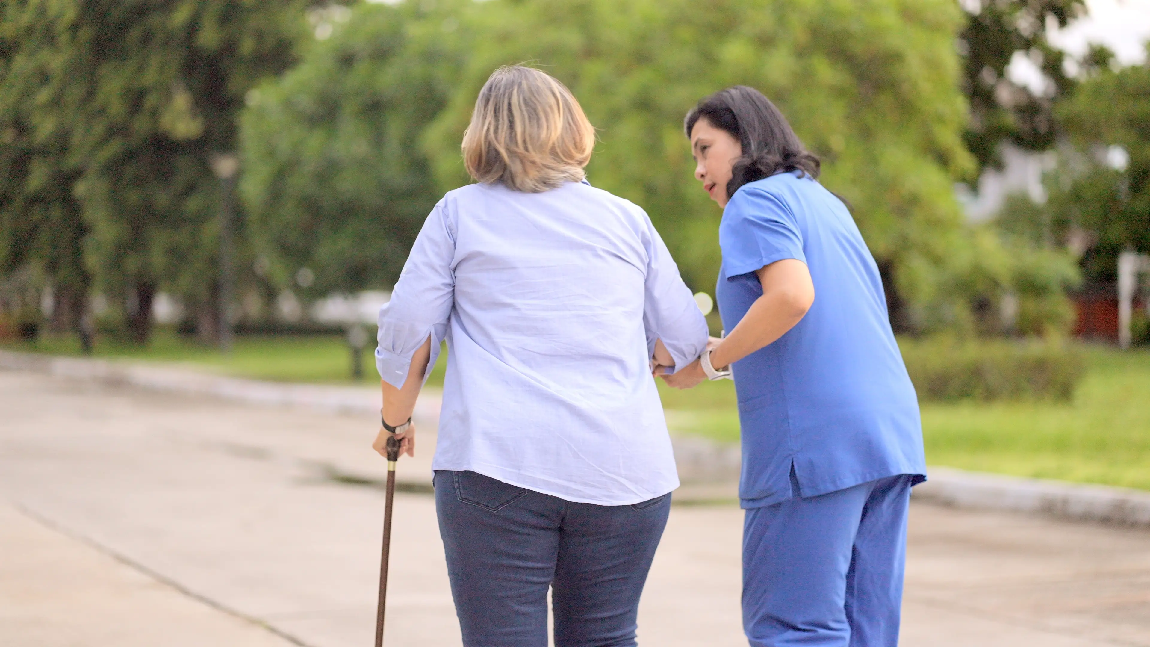 A woman walks with a cane alongside a nurse.