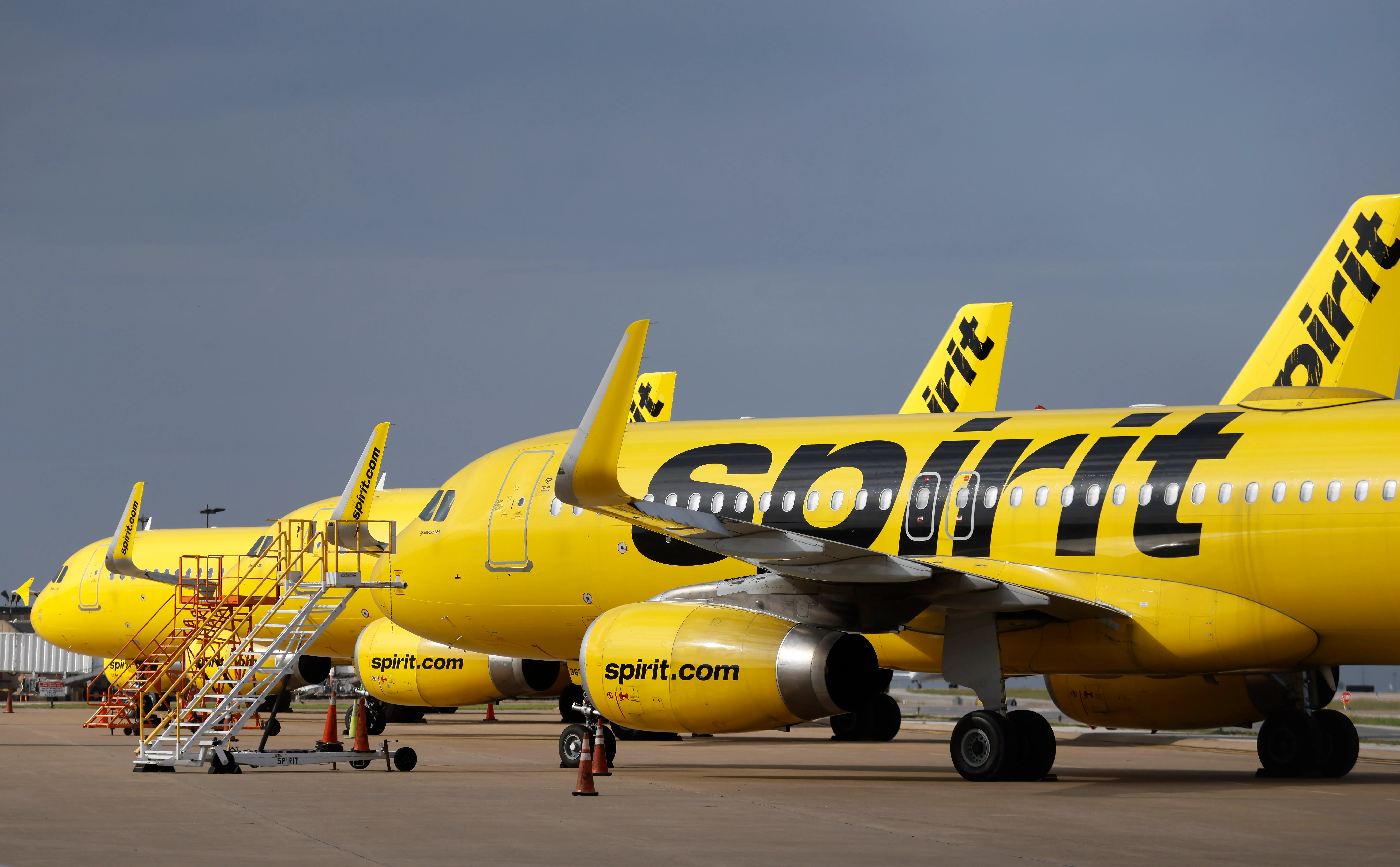 Yellow Spirit Airlines jets are parked in a row on an airport tarmac with mobile stairs beside one aircraft.