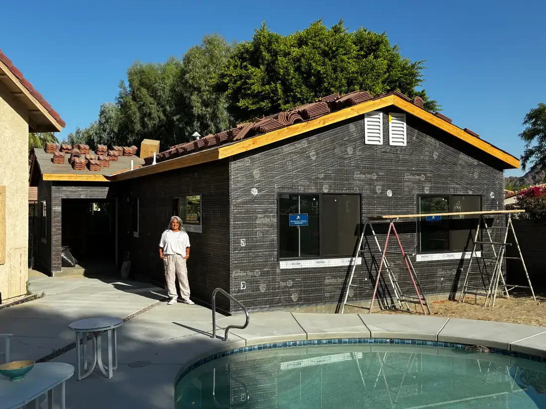 A woman stands next to an ADU under construction, in front of her is the edge of a pool.