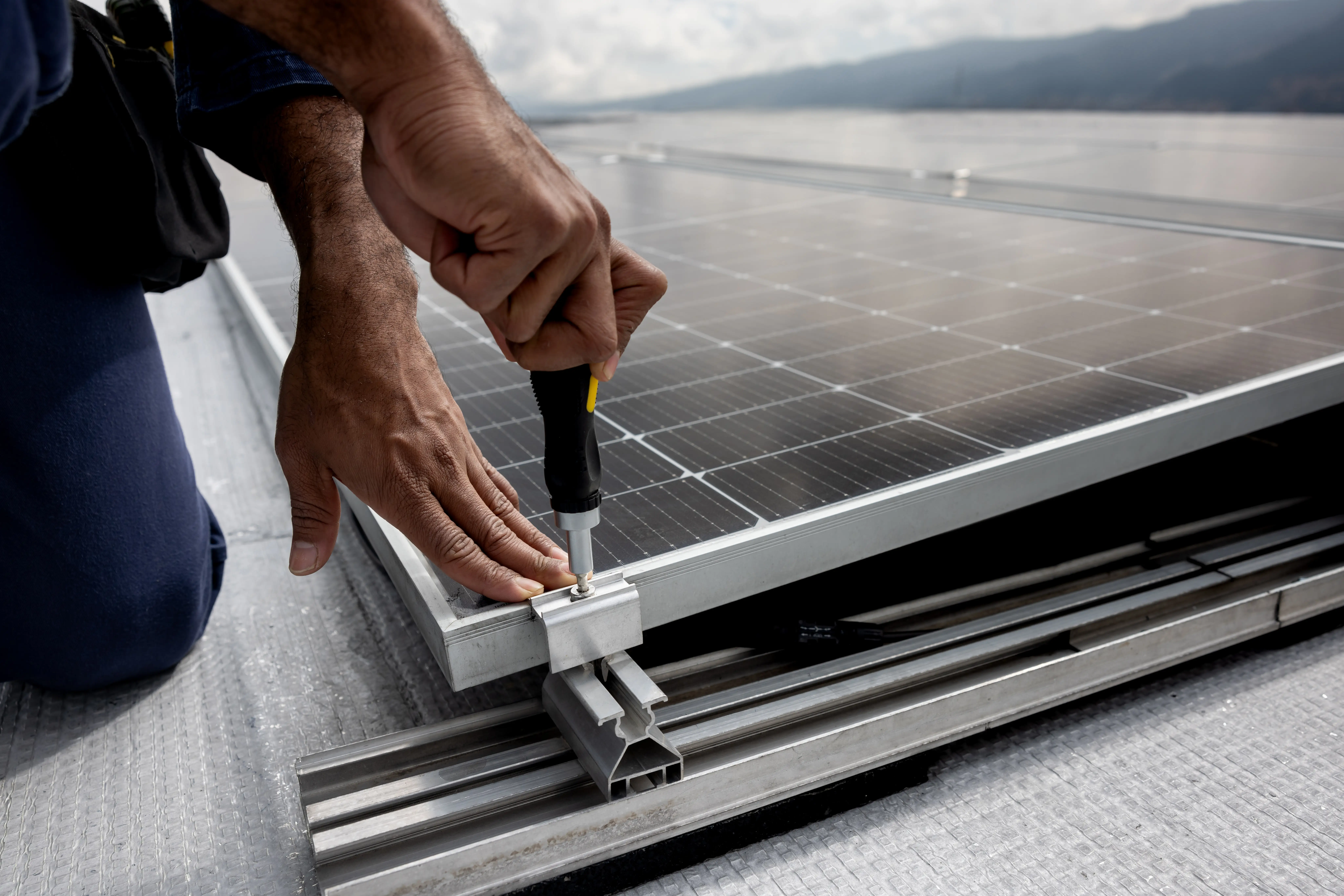 A man's hand screws in the corner of a solar panel.