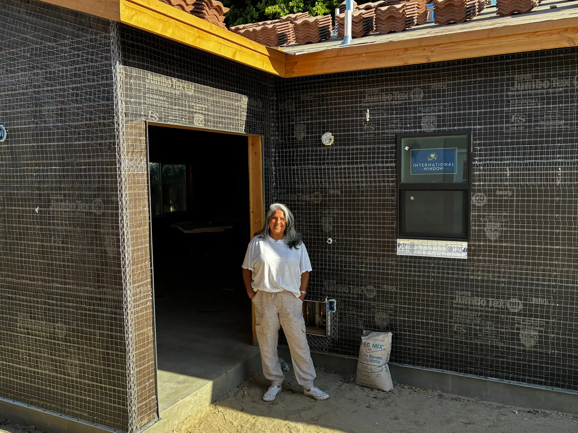A woman stands next to a tiny home that has yet to have its walls plastered.