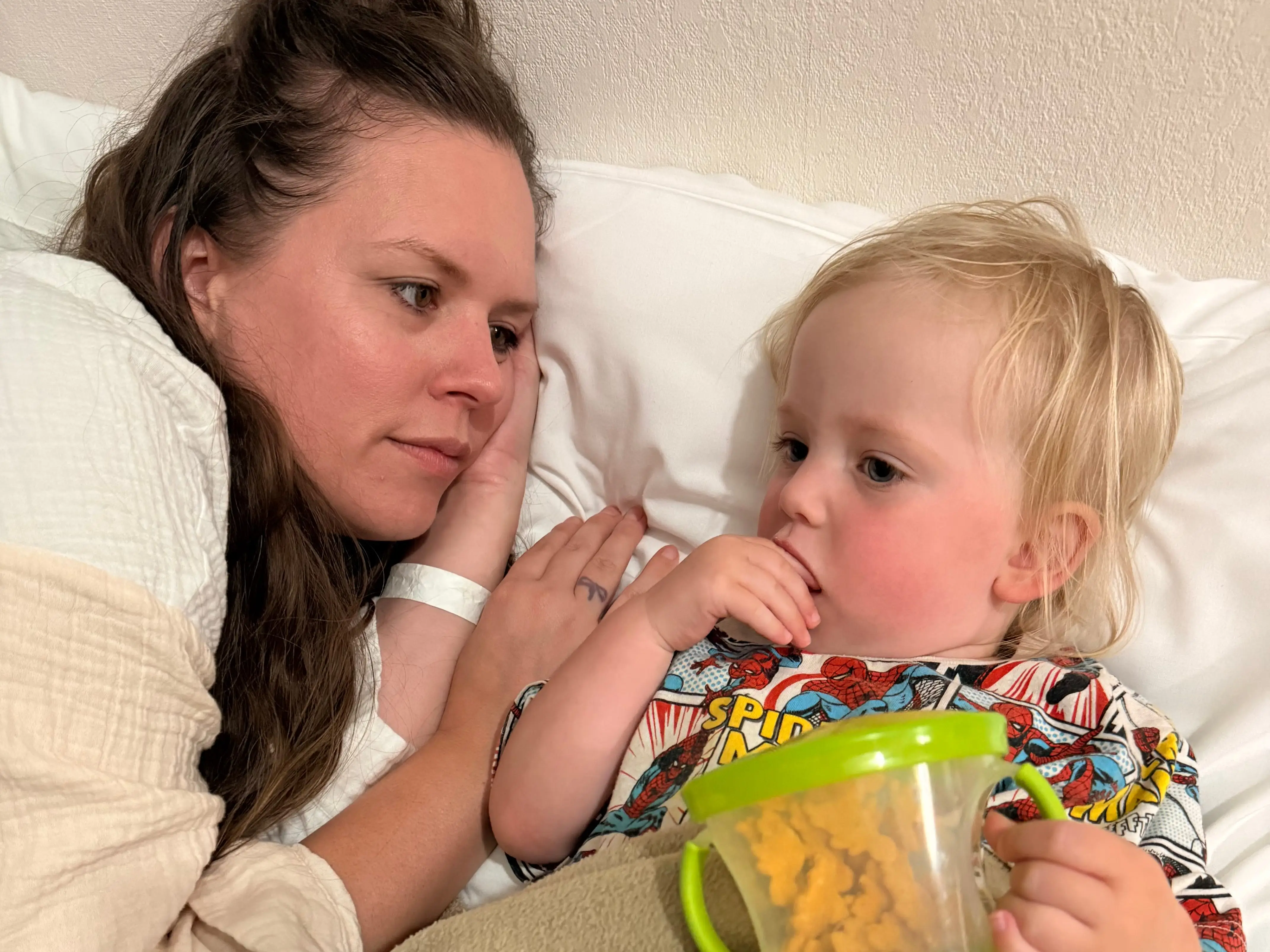 The writer rests a head on a white pillow next to a small child holding a snack container.