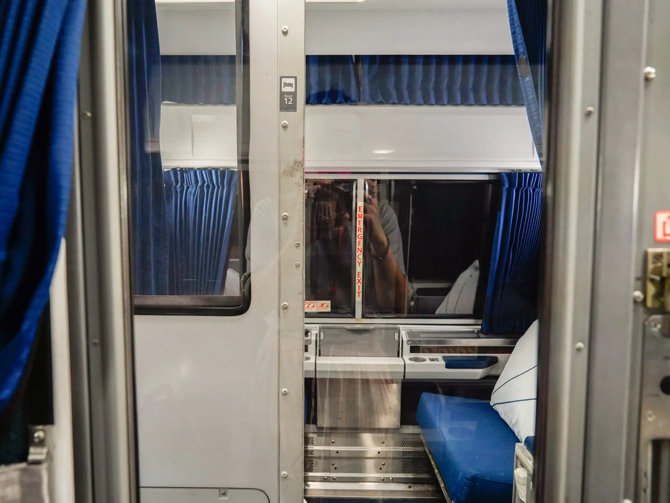 A view of an empty roomette with blue seating and curtains on an Amtrak overnight train