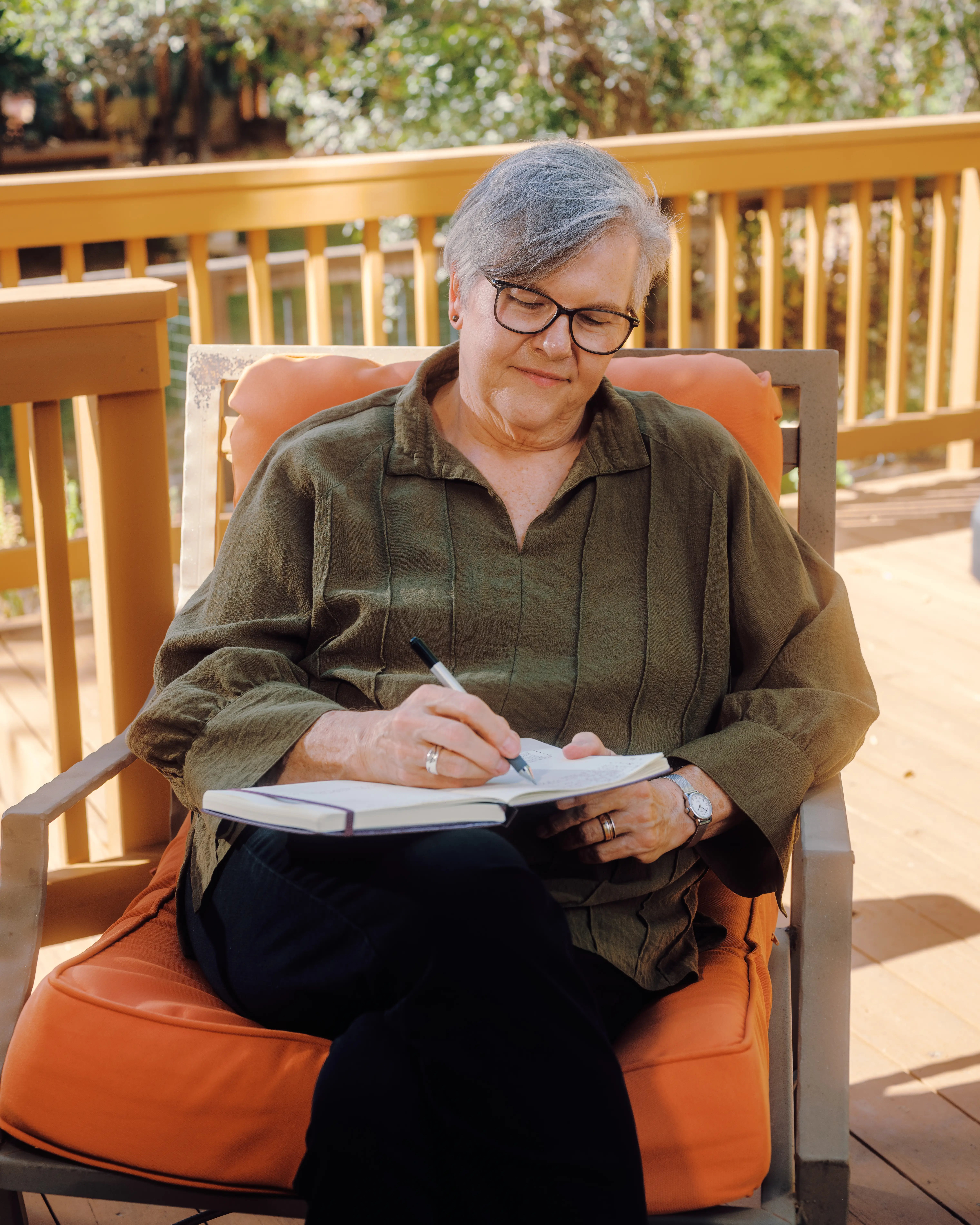 Becky writes in a notebook while seated on an outdoor deck chair.