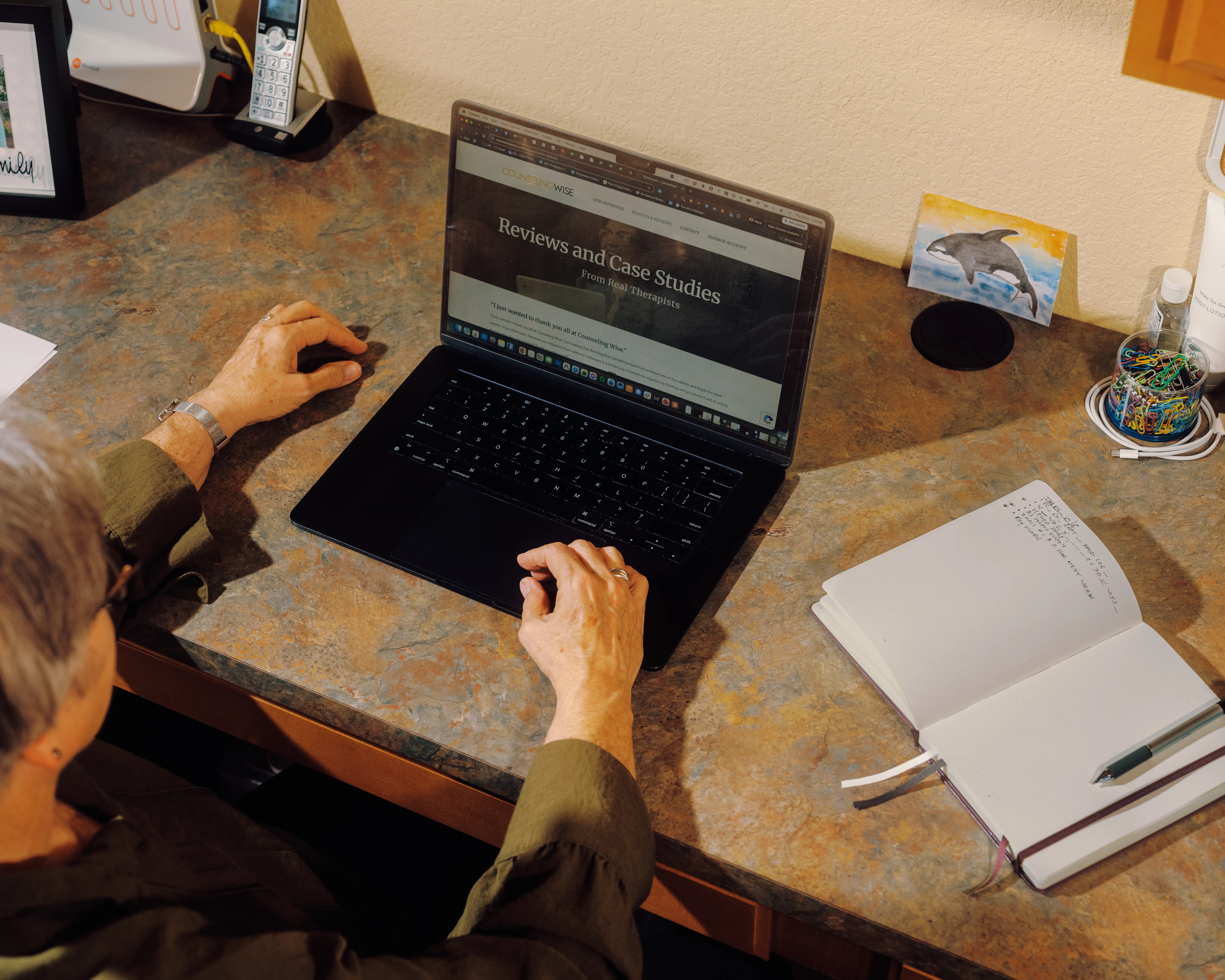 Becky uses a laptop showing a reviews and case studies webpage beside an open notebook on a desk.