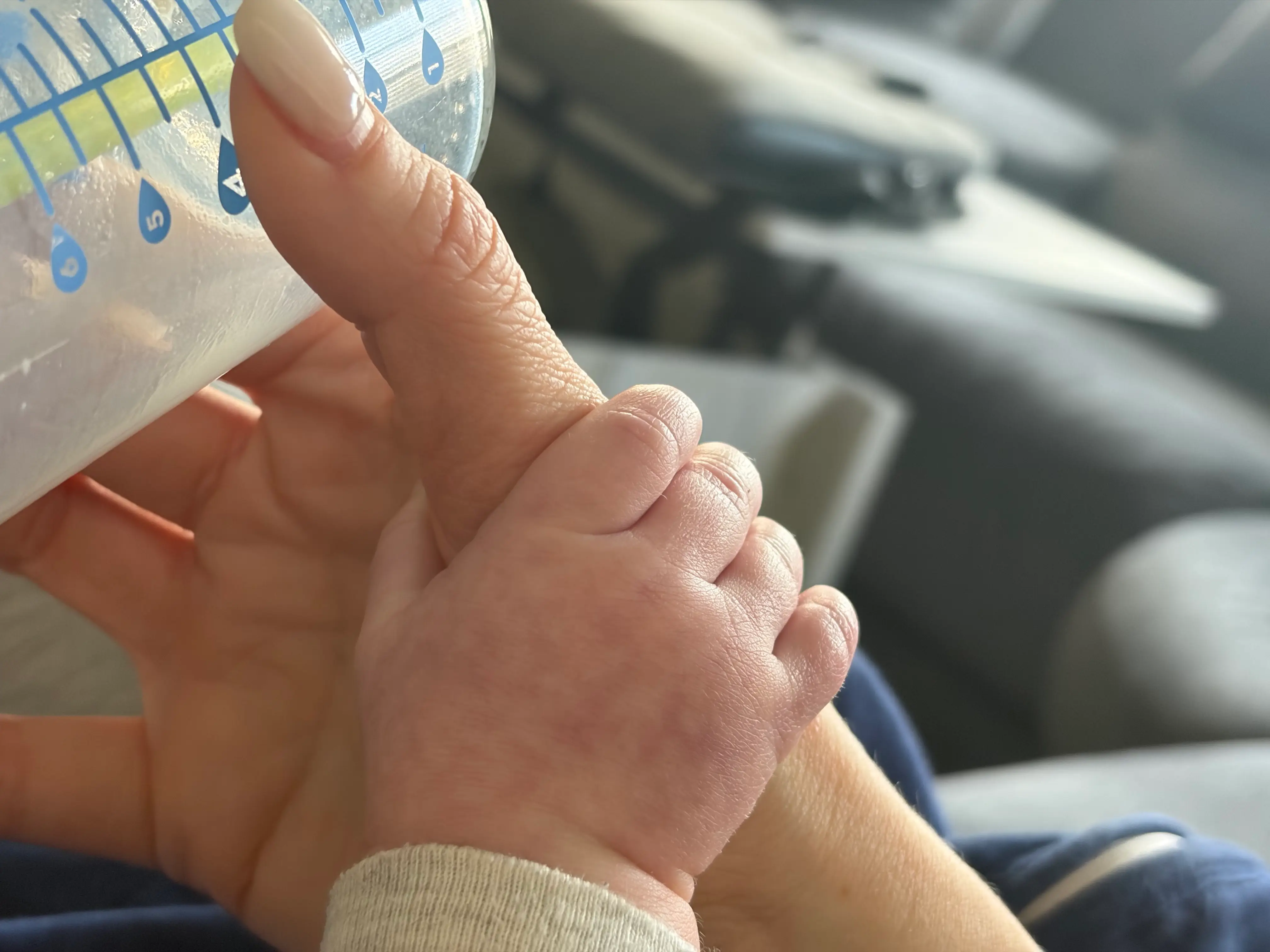 close up of baby's hand holding mother's during bottle-feeding