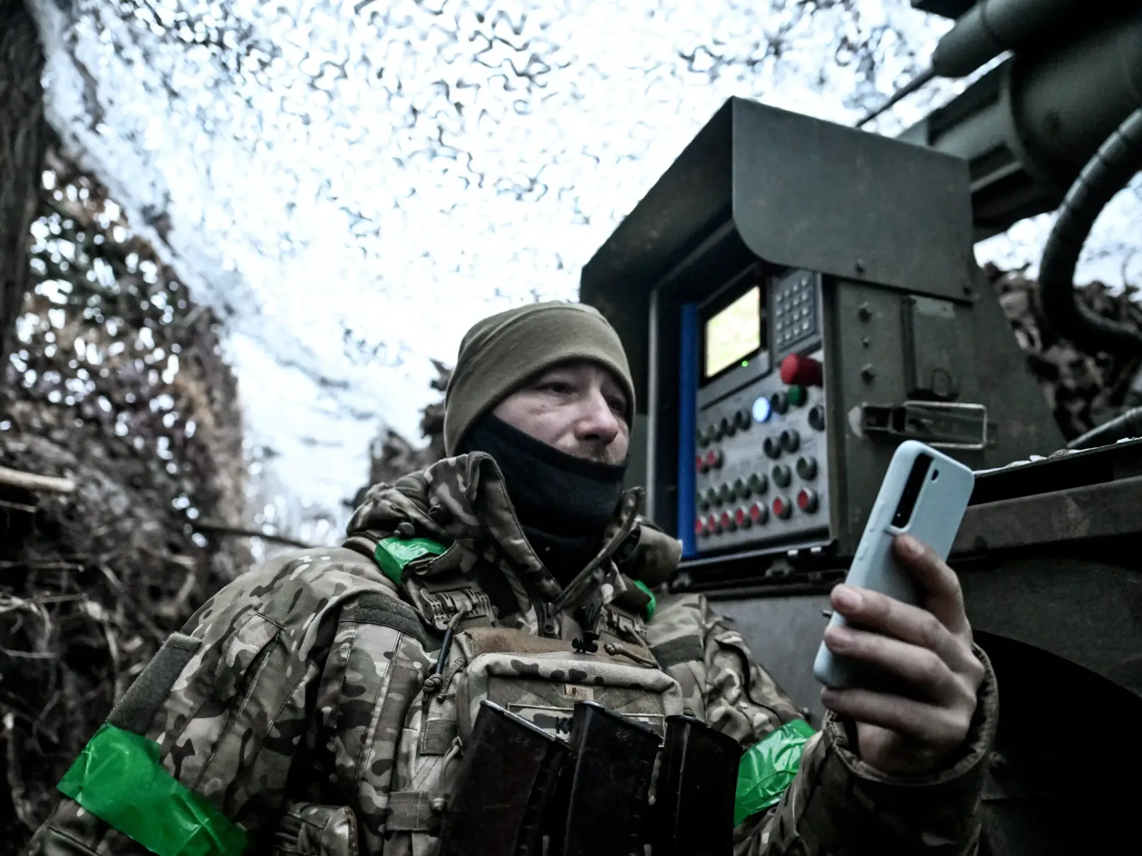 Soldier uses phone under camo netting.