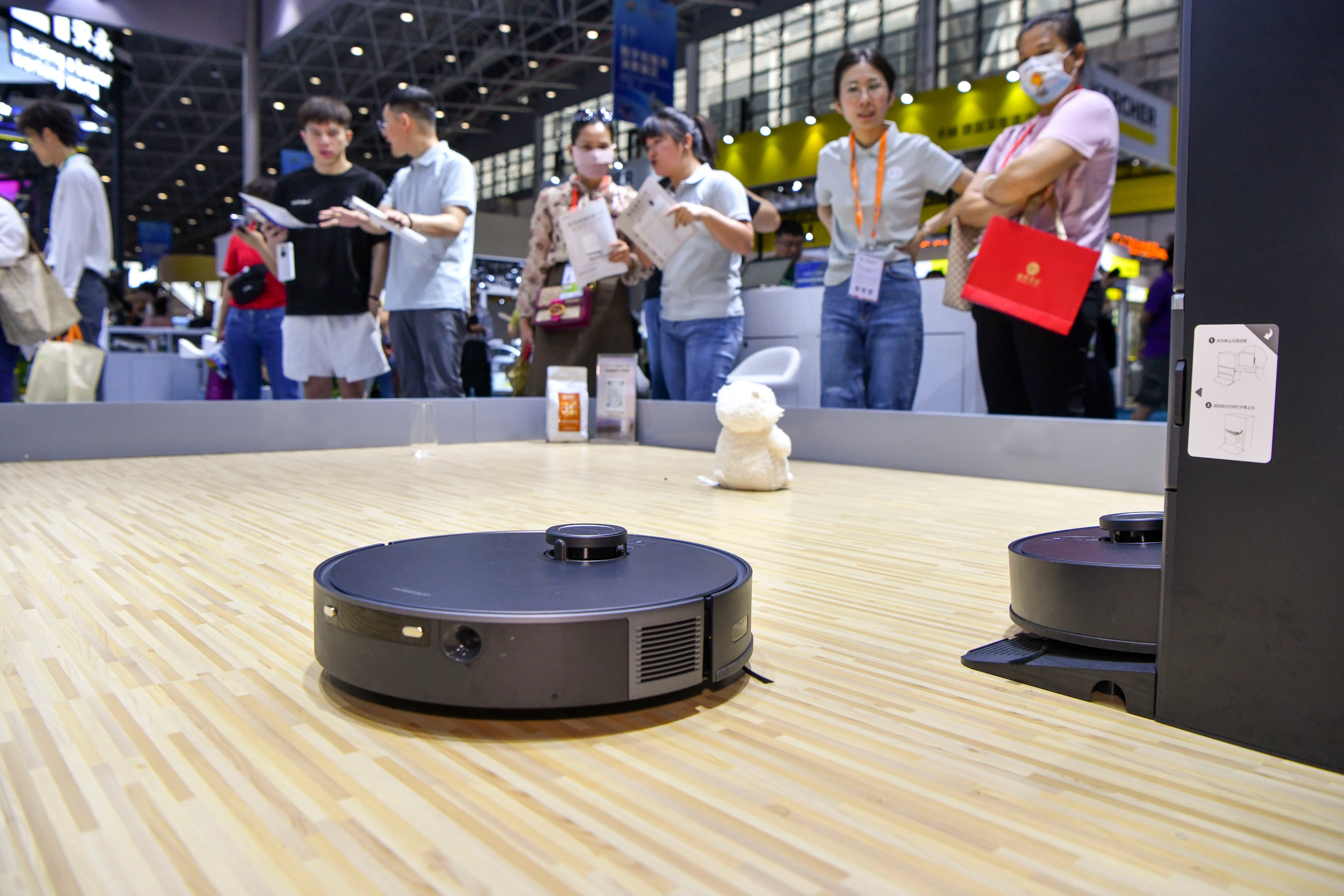 Visitors are attracted by an AI sweeping robot during a Consumer Products Expo in Hainan.