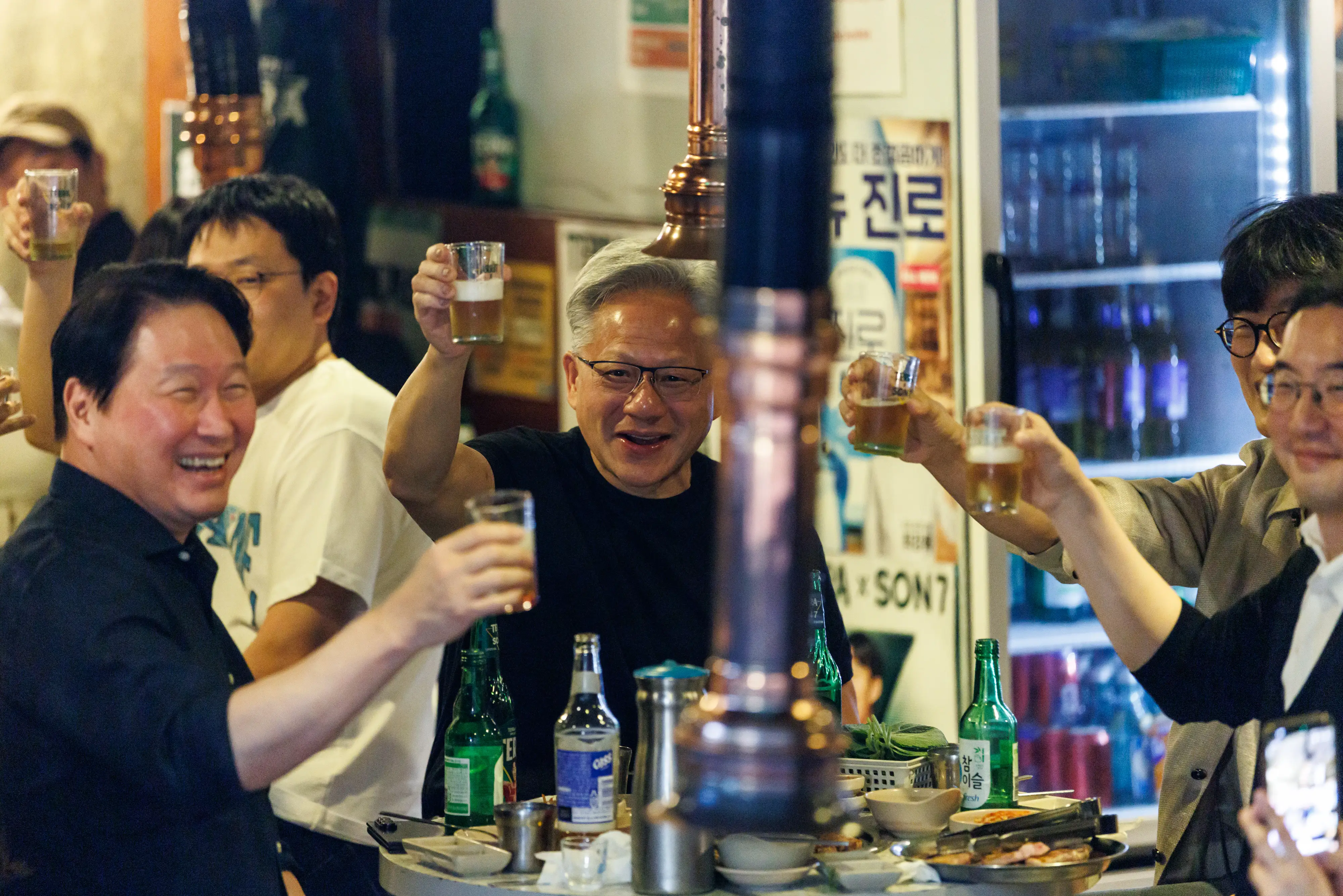 Jensen Huang and other diners raise glasses around a restaurant table with bottles and a barbecue exhaust pipe.