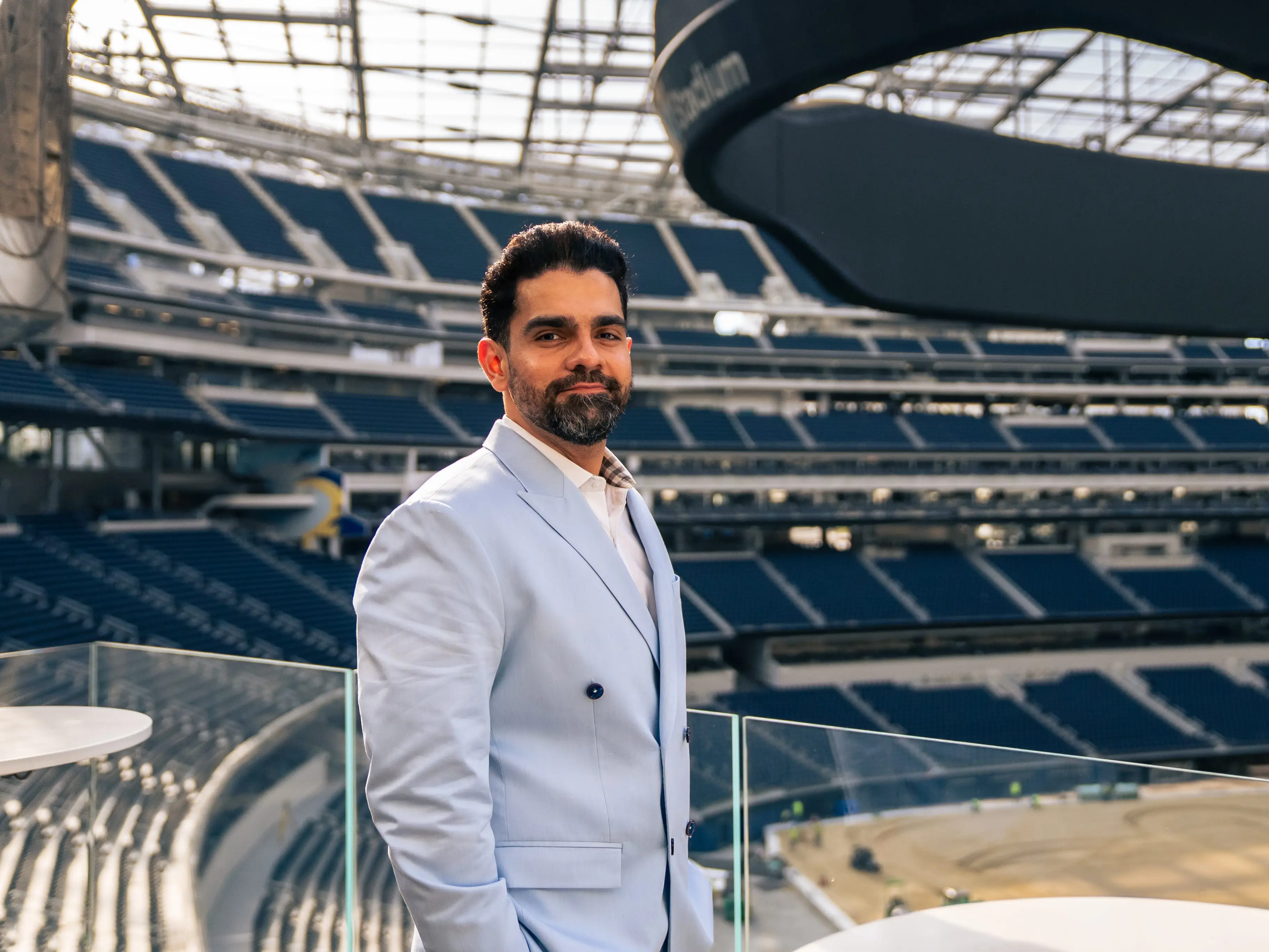 Hardik Jagda is wearing a light blue suit and standing inside a stadium.