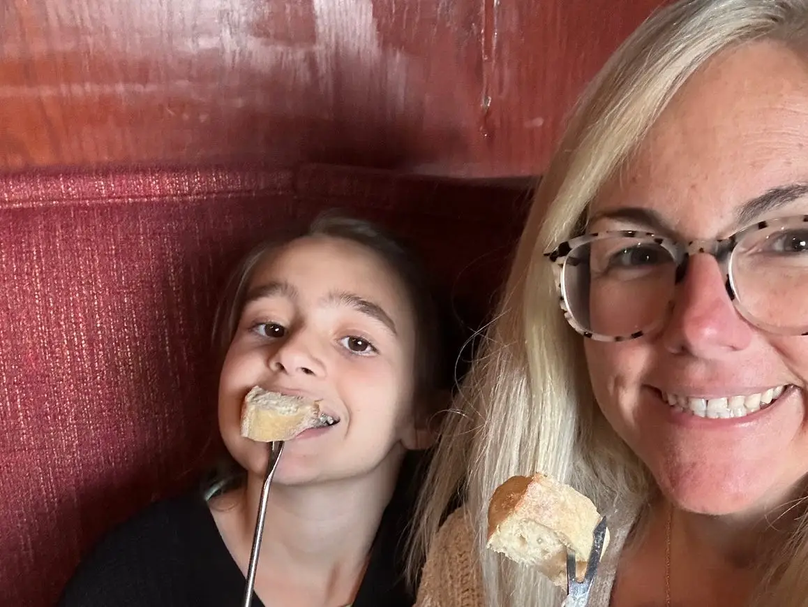Two people smile in a restaurant booth while holding fondue forks with pieces of bread.