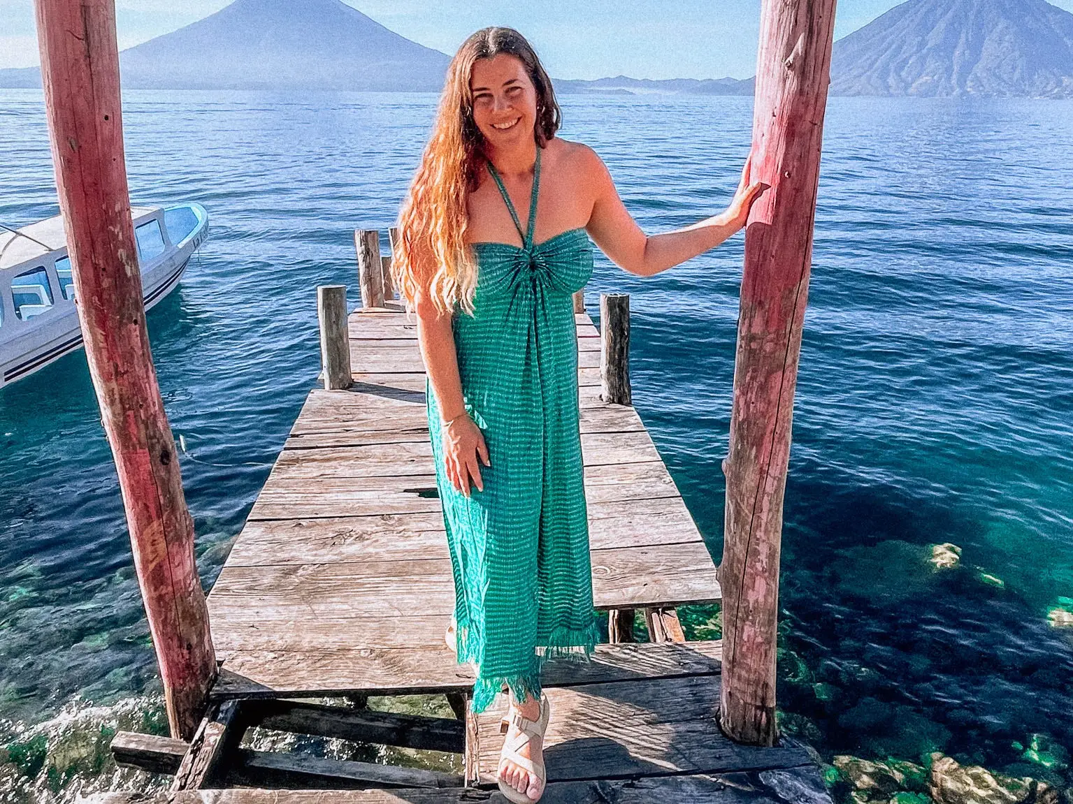Jackie poses for a photo near a boat dock, with mountains in the background.