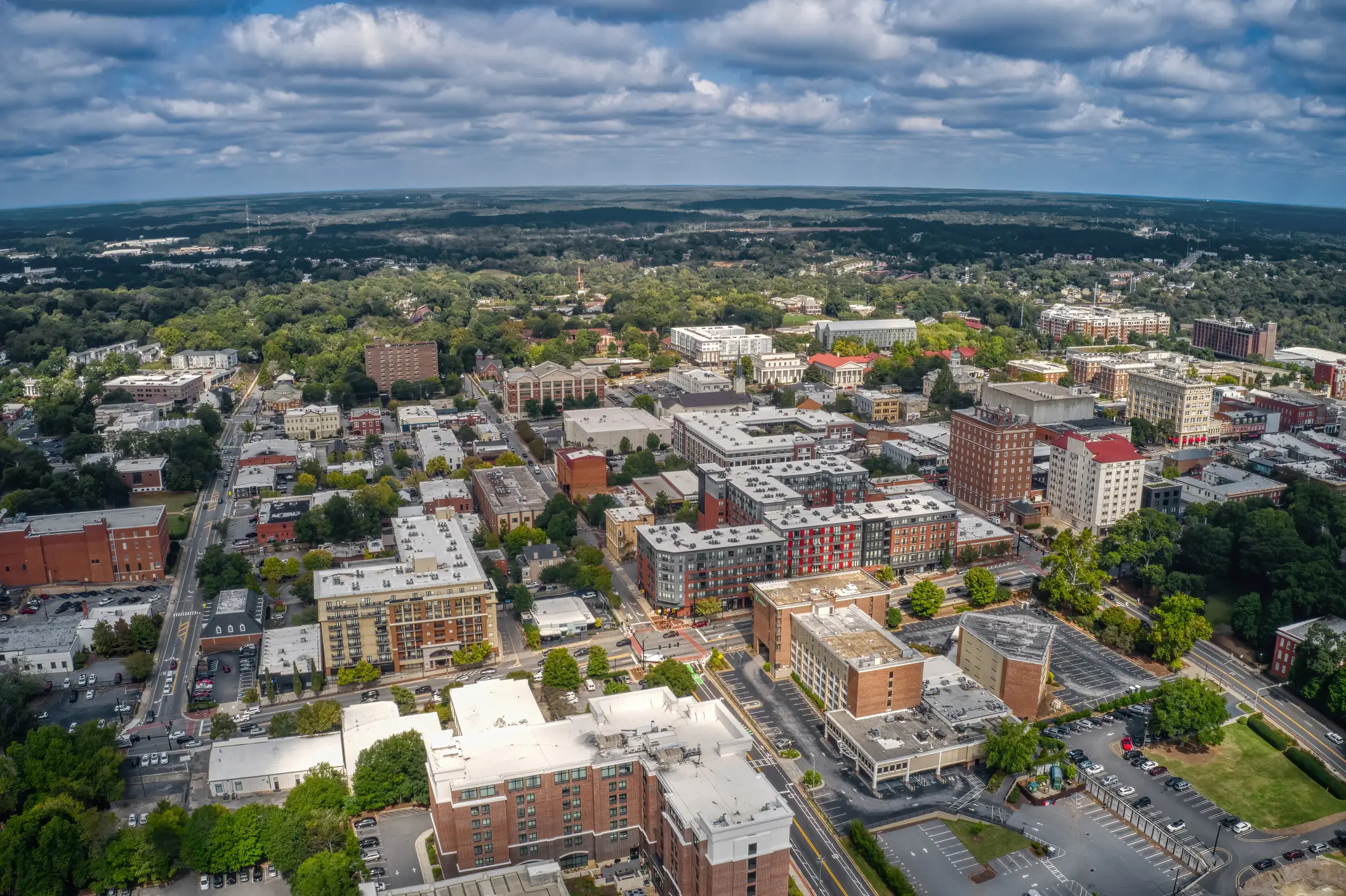 Aerial view of a dense urban downtown with roads, brick buildings, trees, and cloudy sky.