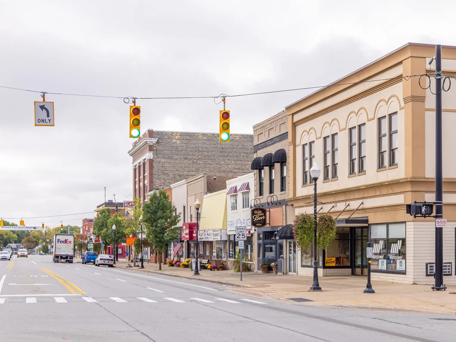 Downtown street lined with storefronts, traffic lights, and vehicles under a cloudy sky.
