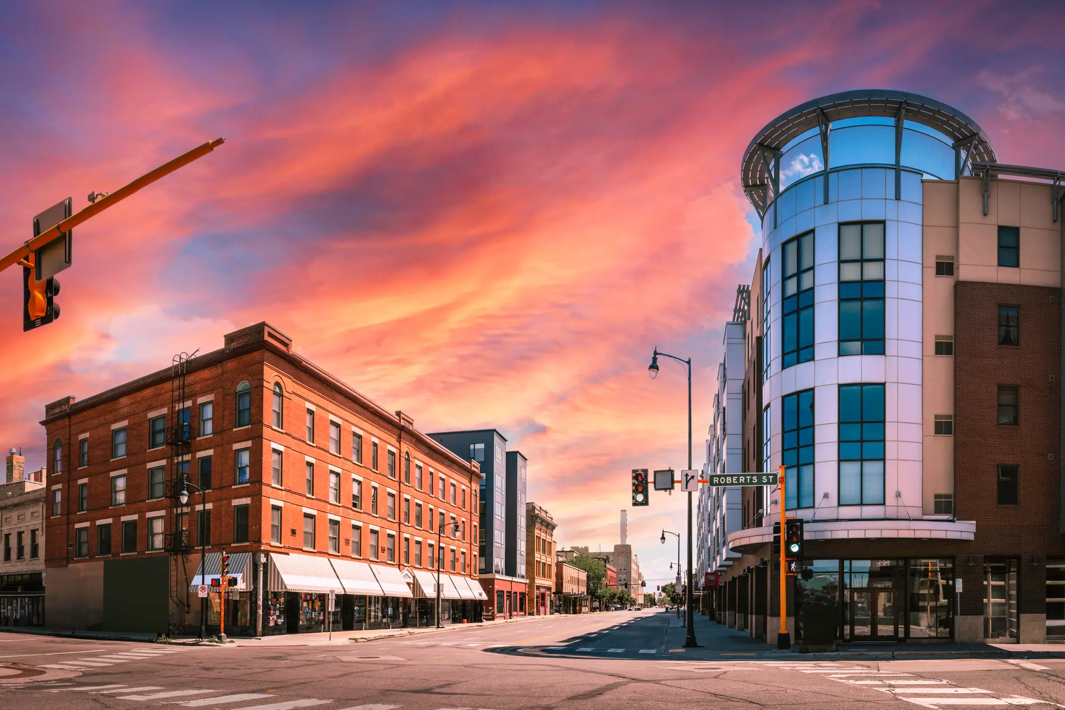 Downtown intersection with brick and glass buildings under a vivid pink and orange sunset sky.