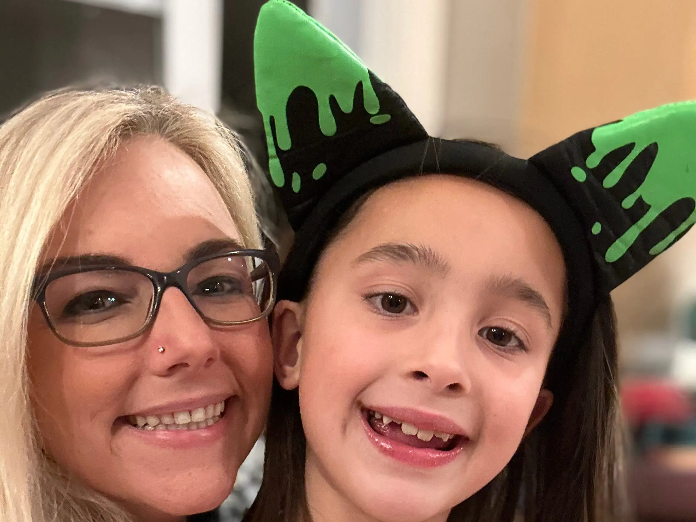 Two smiling people pose indoors, one wearing a black headband with green cat ears.