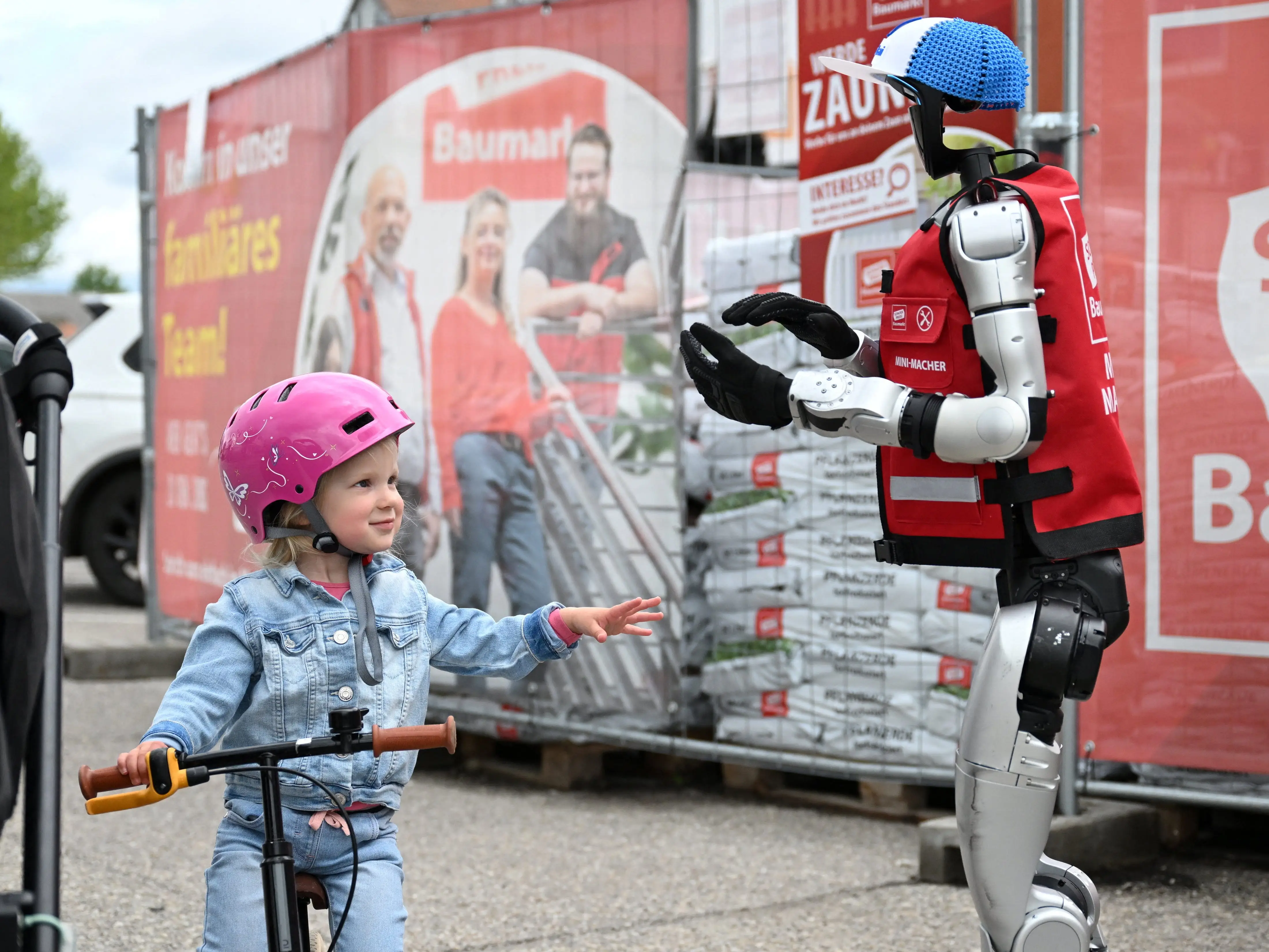 A toddler reaches her hand out to a humanoid.