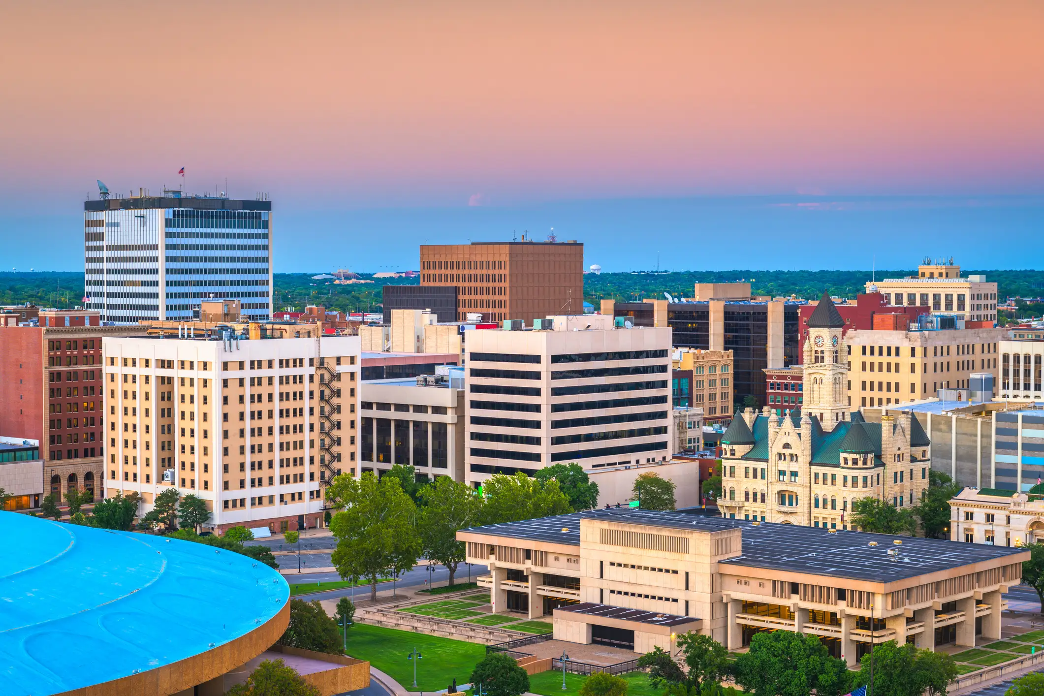 Downtown Fort Wayne skyline with office buildings and the Allen County Courthouse under a pink and blue dusk sky.