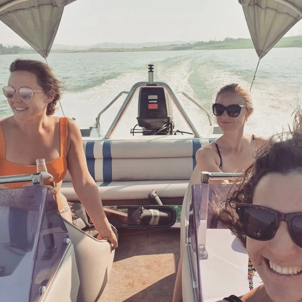 Three people wearing sunglasses ride in a speedboat leaving a wake across a wide lake.