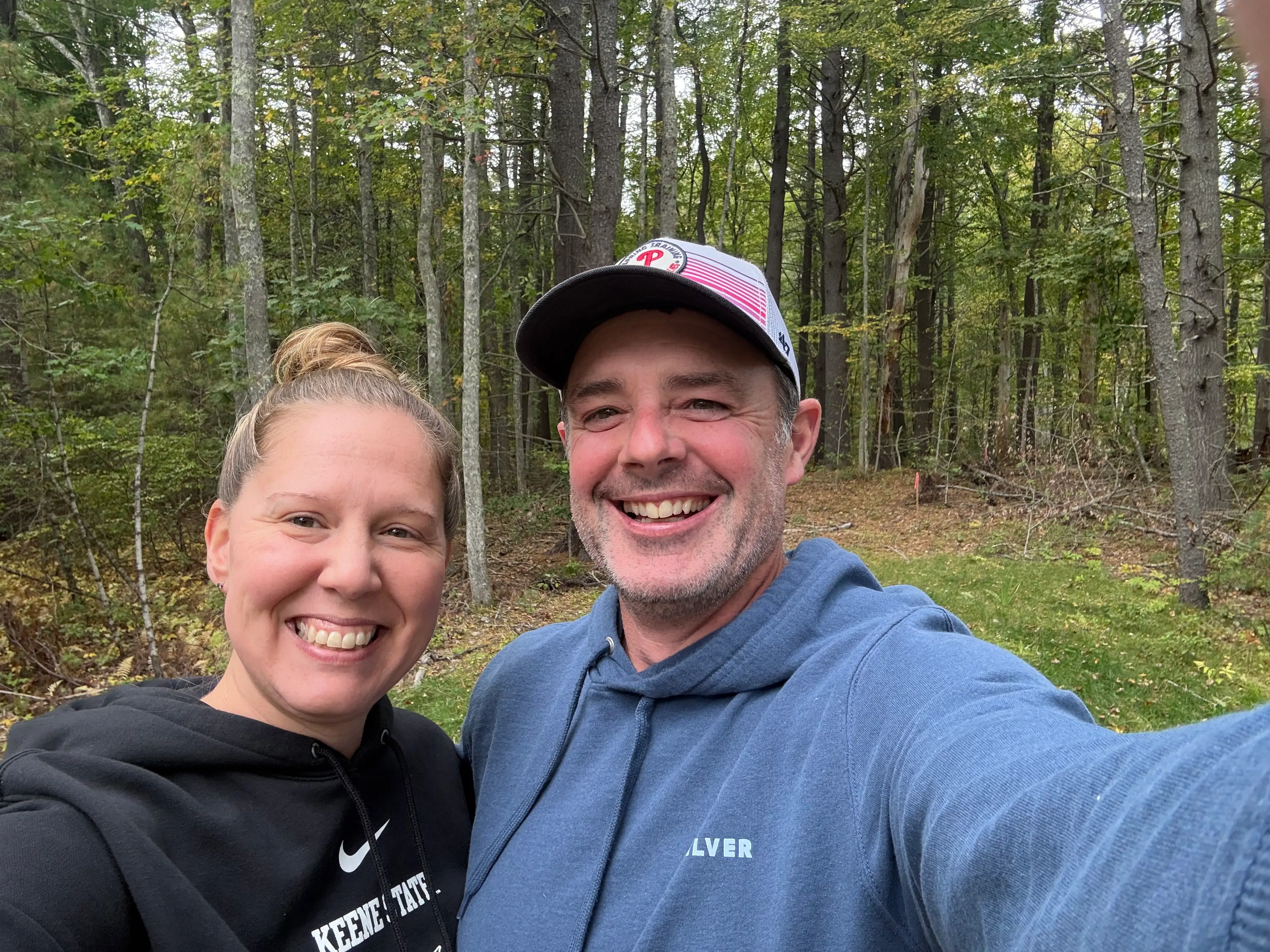 The writer and her husband smile for the camera while standing in front of rural land they own in Maine.