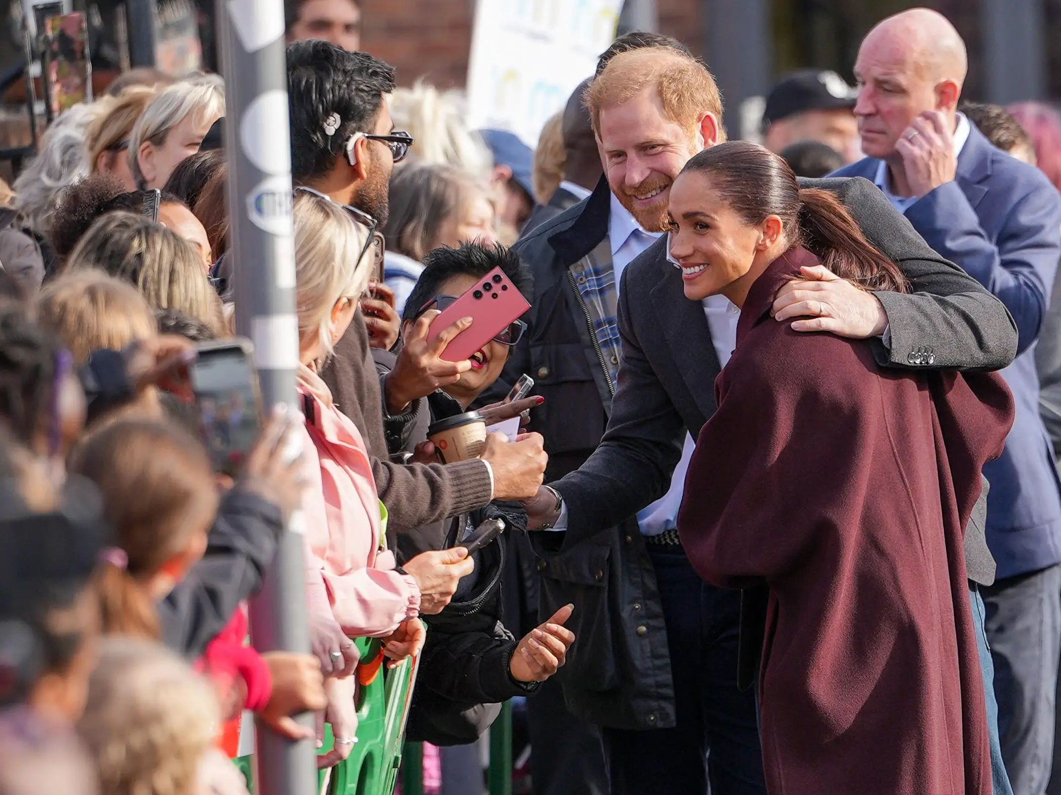 Prince Harry and Meghan Markle greet a crowd behind barriers during a public outdoor appearance.