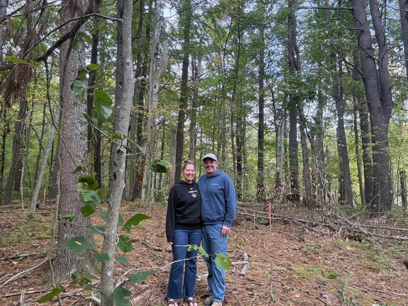 The writer and her husband posing in front of trees on their land in Maine.