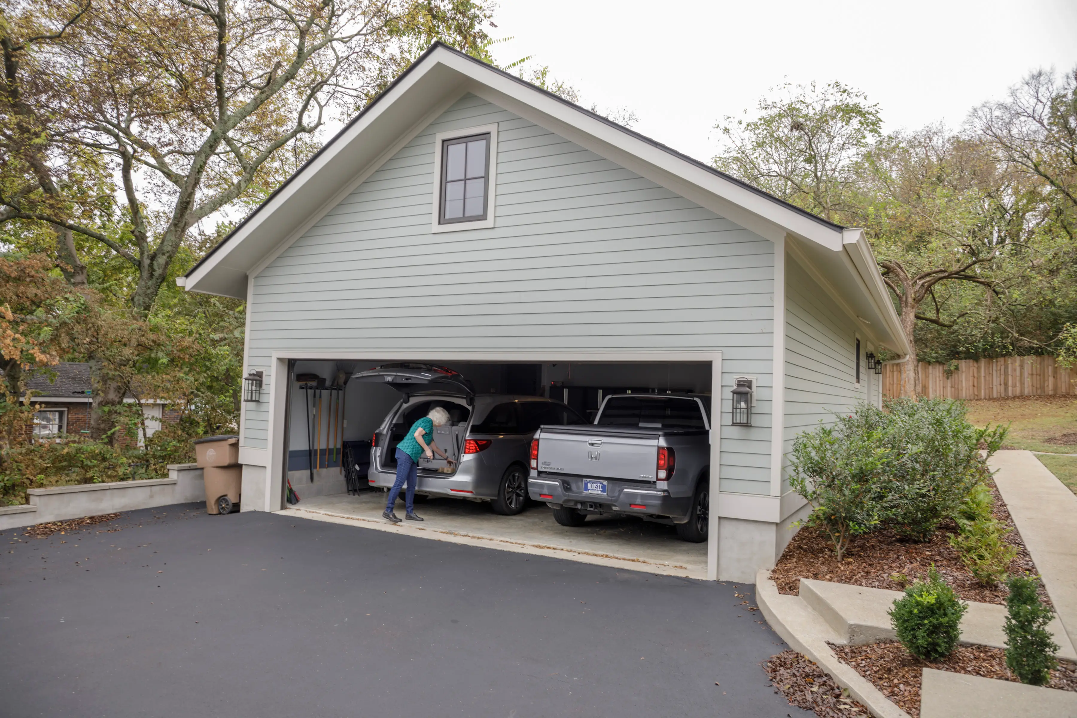 Detached two-car garage with an open door, two vehicles inside, and a person loading items into a minivan.