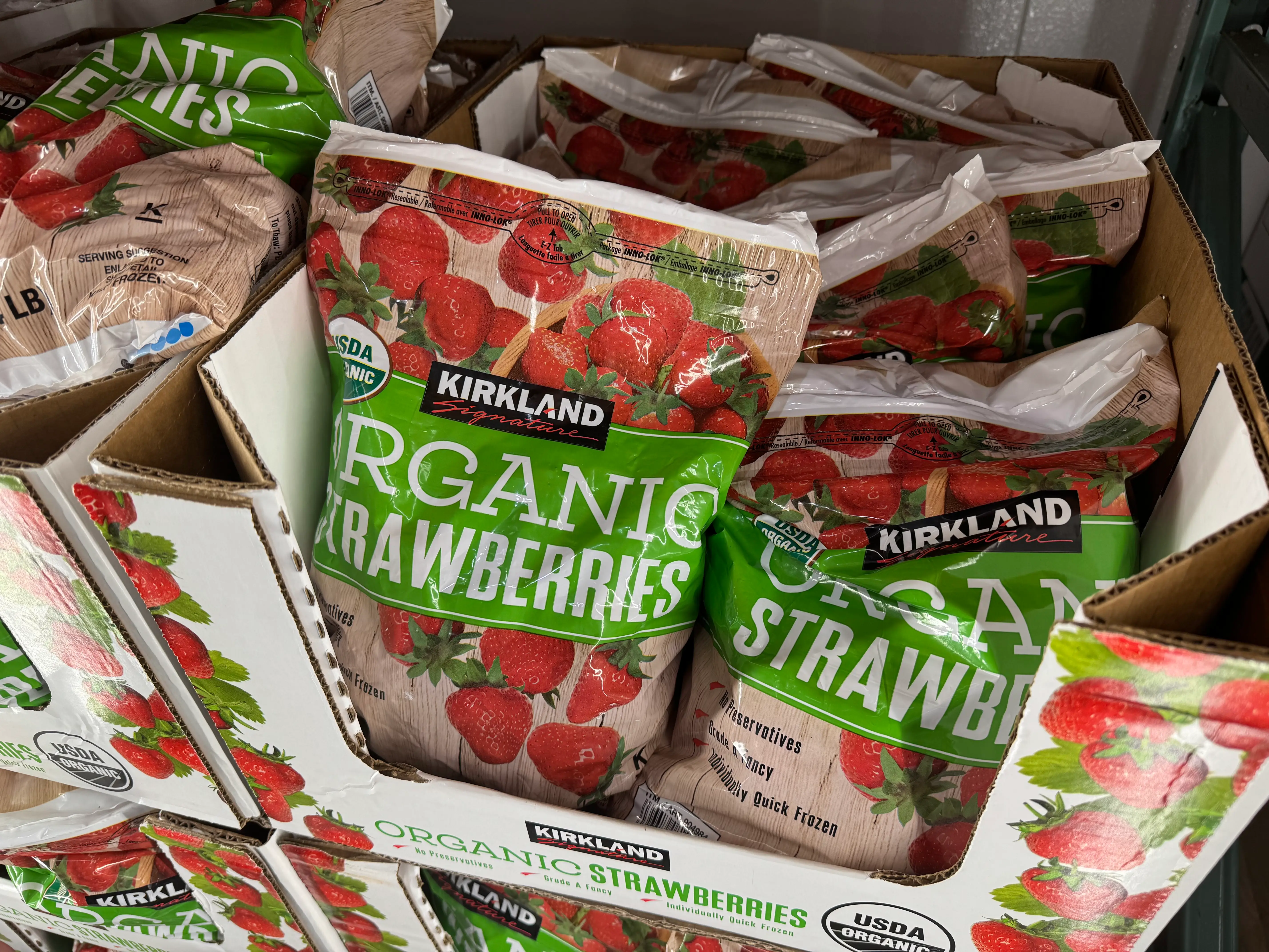 Packages of KIRKLAND Signature ORGANIC STRAWBERRIES are stacked in cardboard display boxes in a freezer case.
