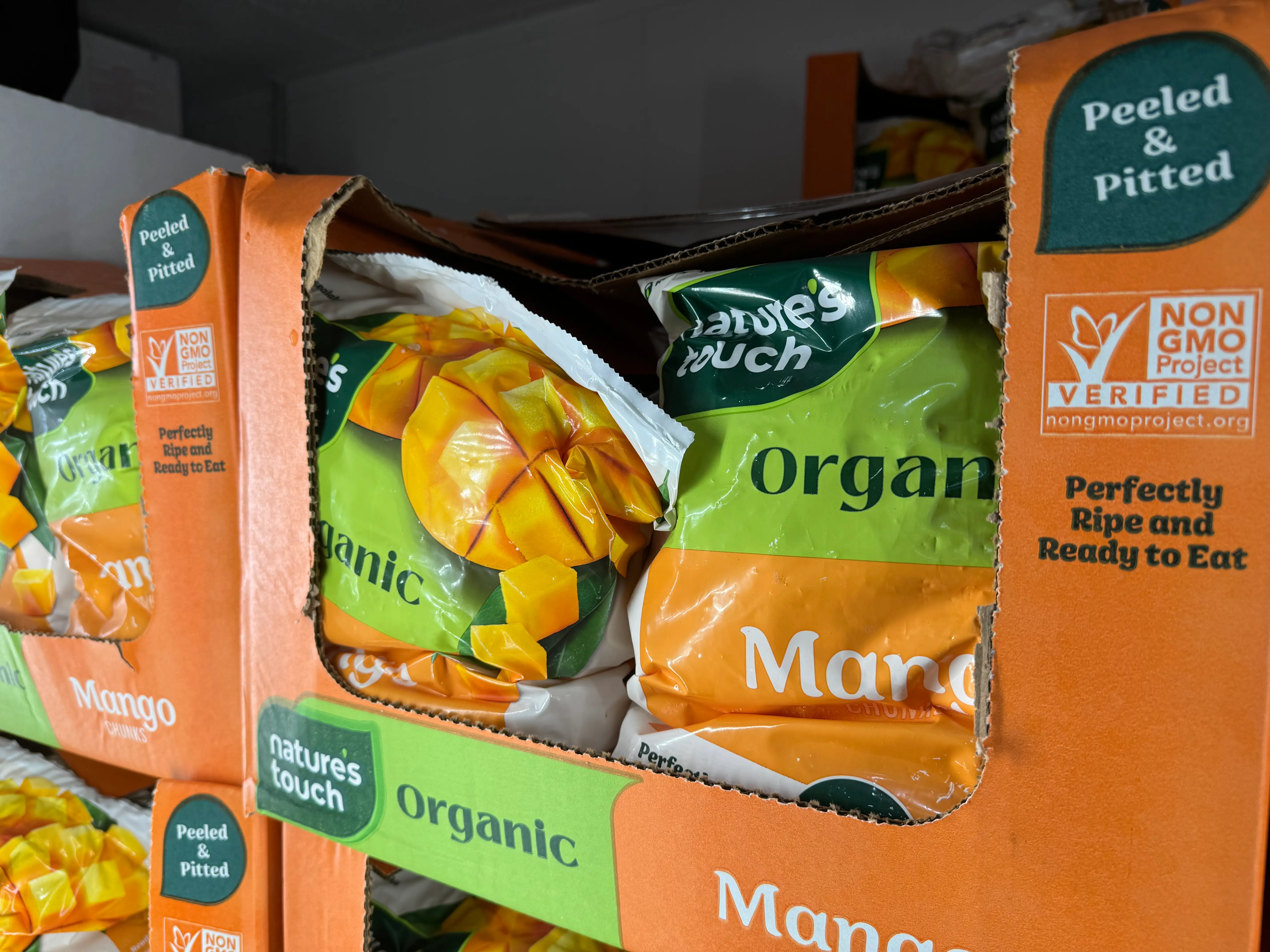 Nature's Touch Organic Mango bags sit in orange cardboard display boxes marked Peeled & Pitted.