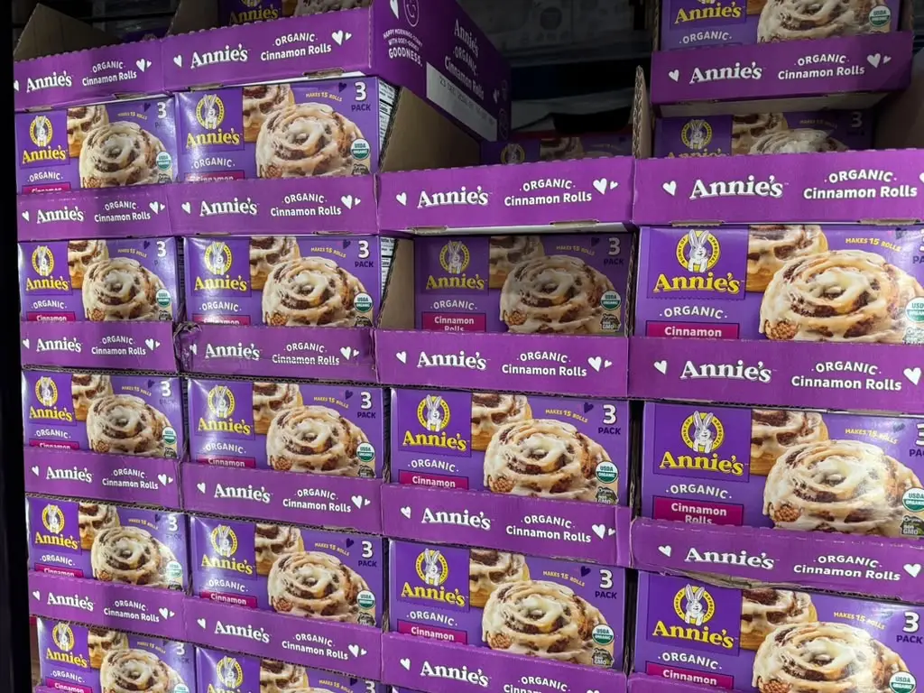Stacks of purple Annie's organic cinnamon rolls multipack boxes are displayed on a store shelf.