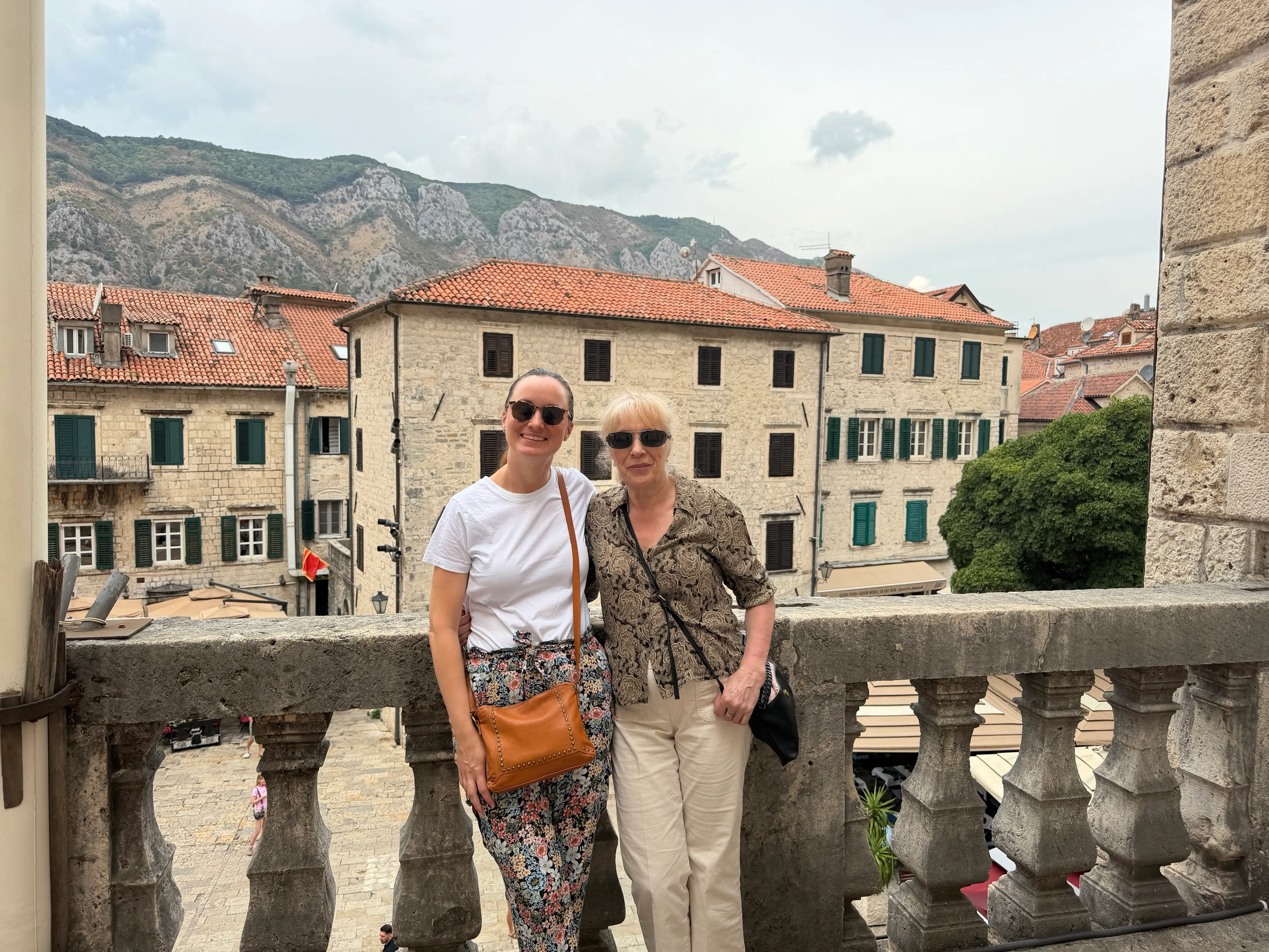 Agnes and her mother pose in front of houses with mountains in the background in Montenegro.