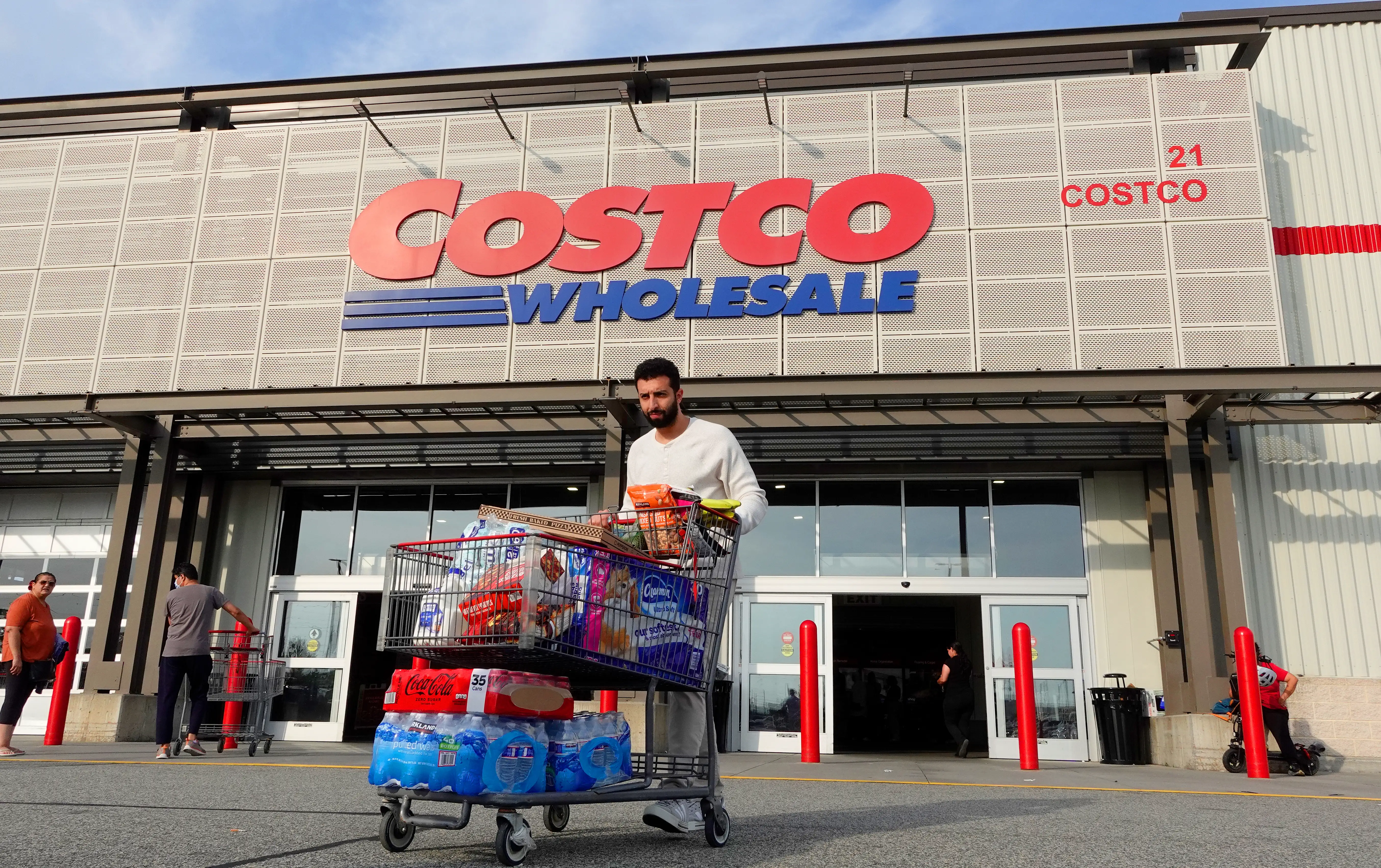 Shopper pushes a loaded cart outside a Costco Wholesale store entrance with large signage overhead.