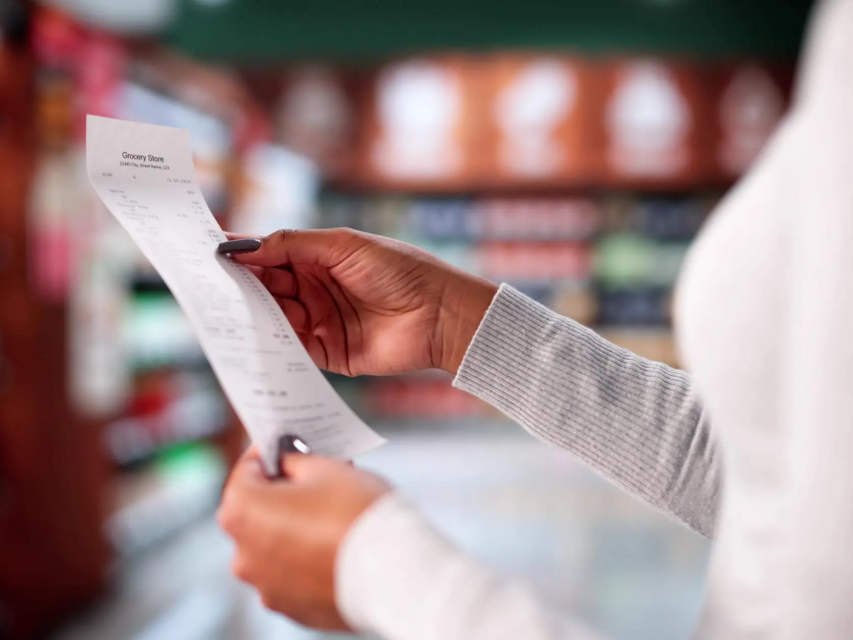 Shopper holds a printed receipt while standing in a blurred grocery store aisle.