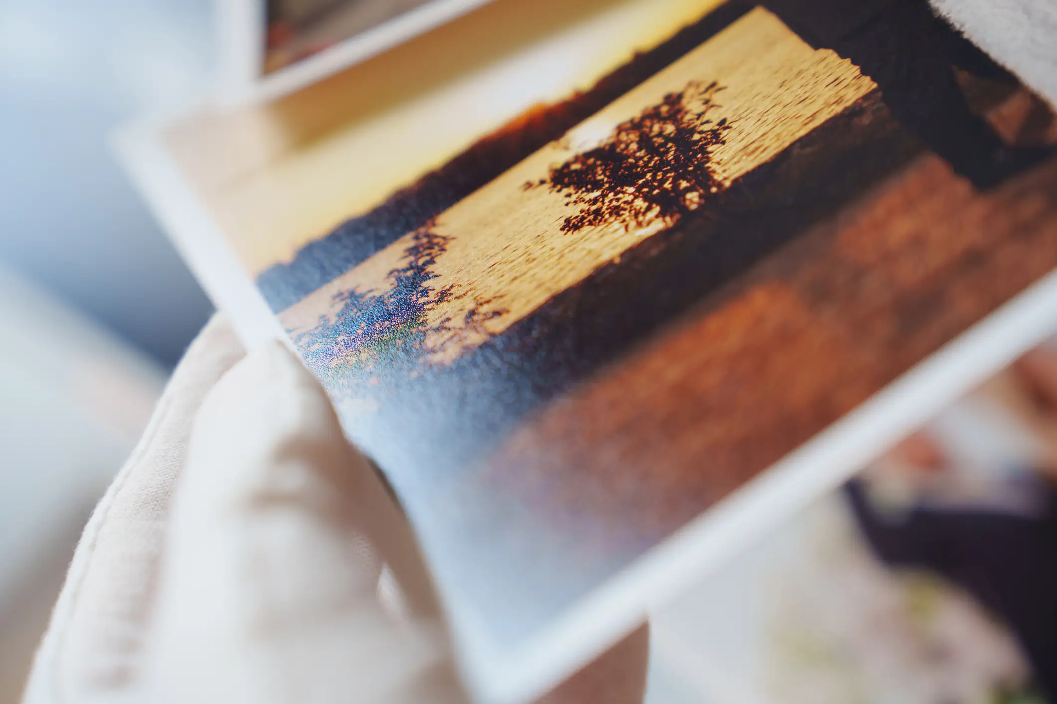 Close-up of a glossy printed photograph showing a sunset landscape with silhouetted trees and water.