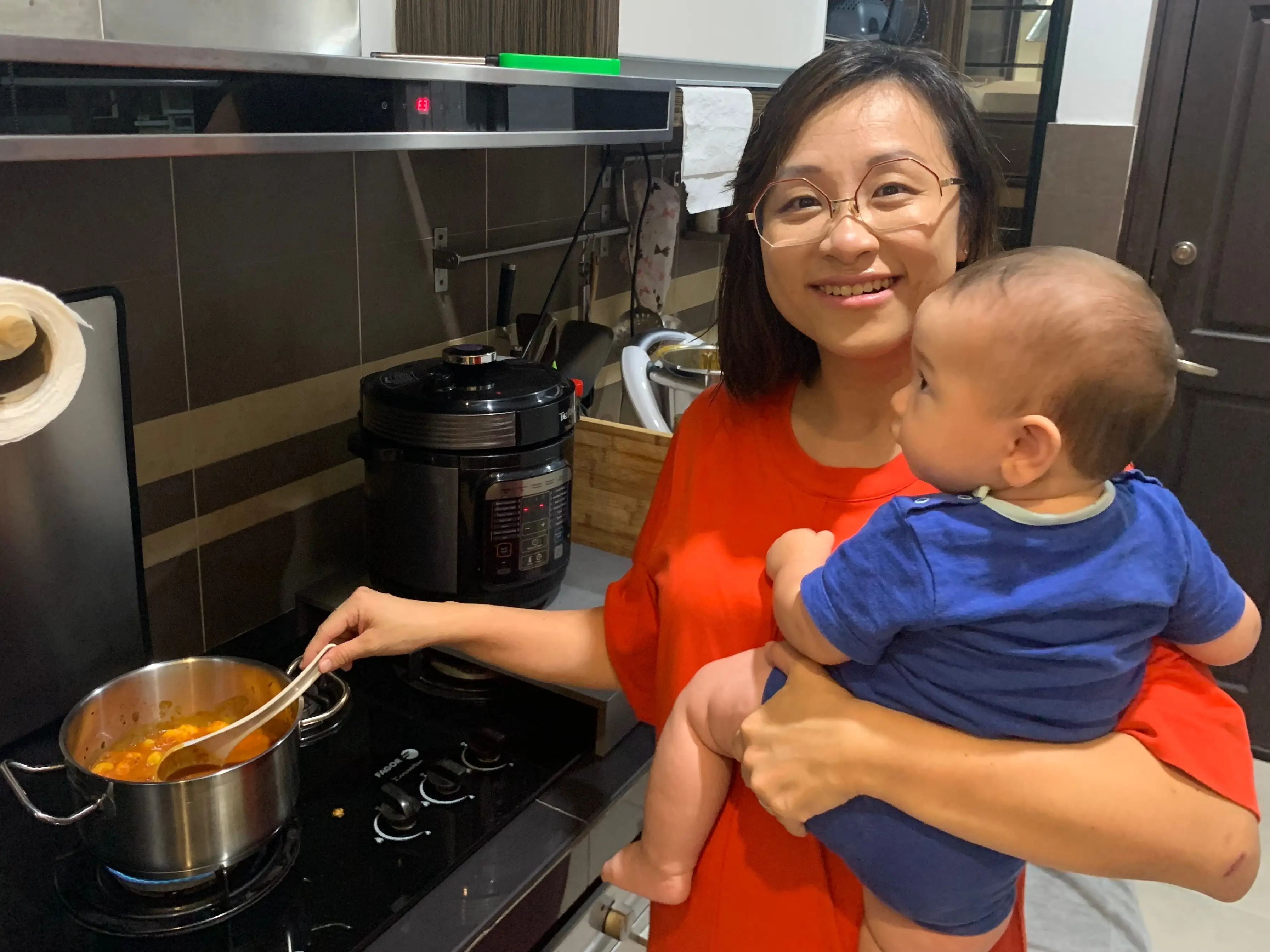 Woman holdng baby stirring food in a pot on stovetop