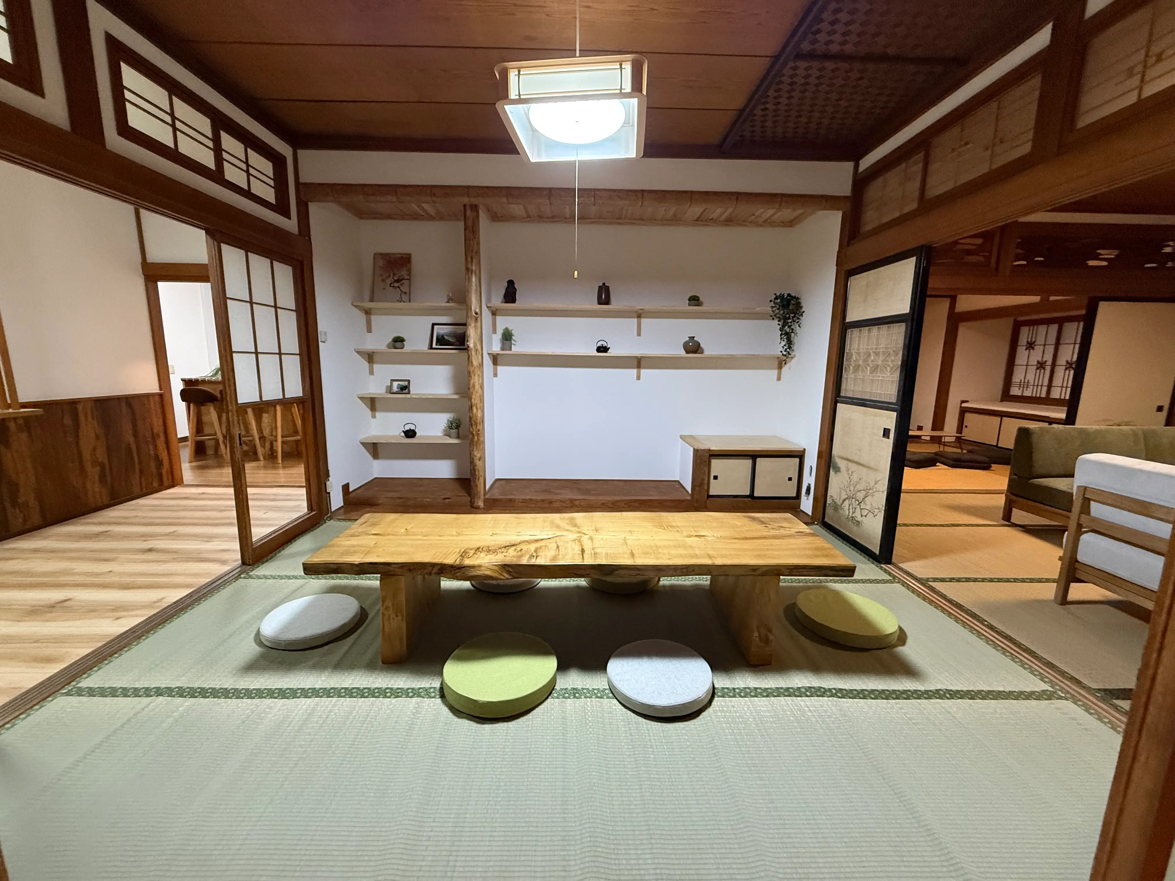 Traditional tatami room with a low wooden table, floor cushions, sliding doors, shelves, and warm wood interior details.