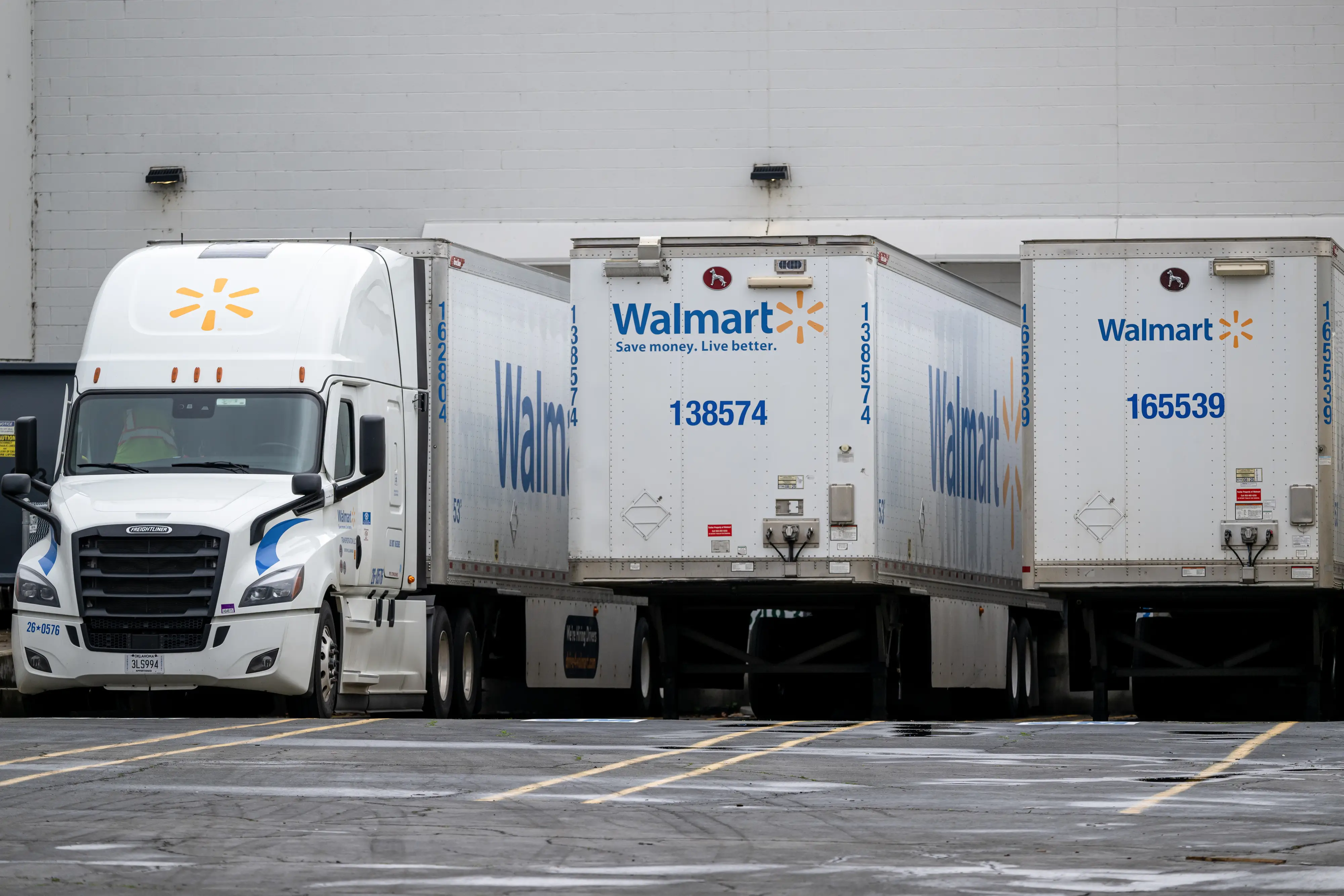 Walmart semi-truck trailers are parked at loading docks beside a white tractor in a wet lot.