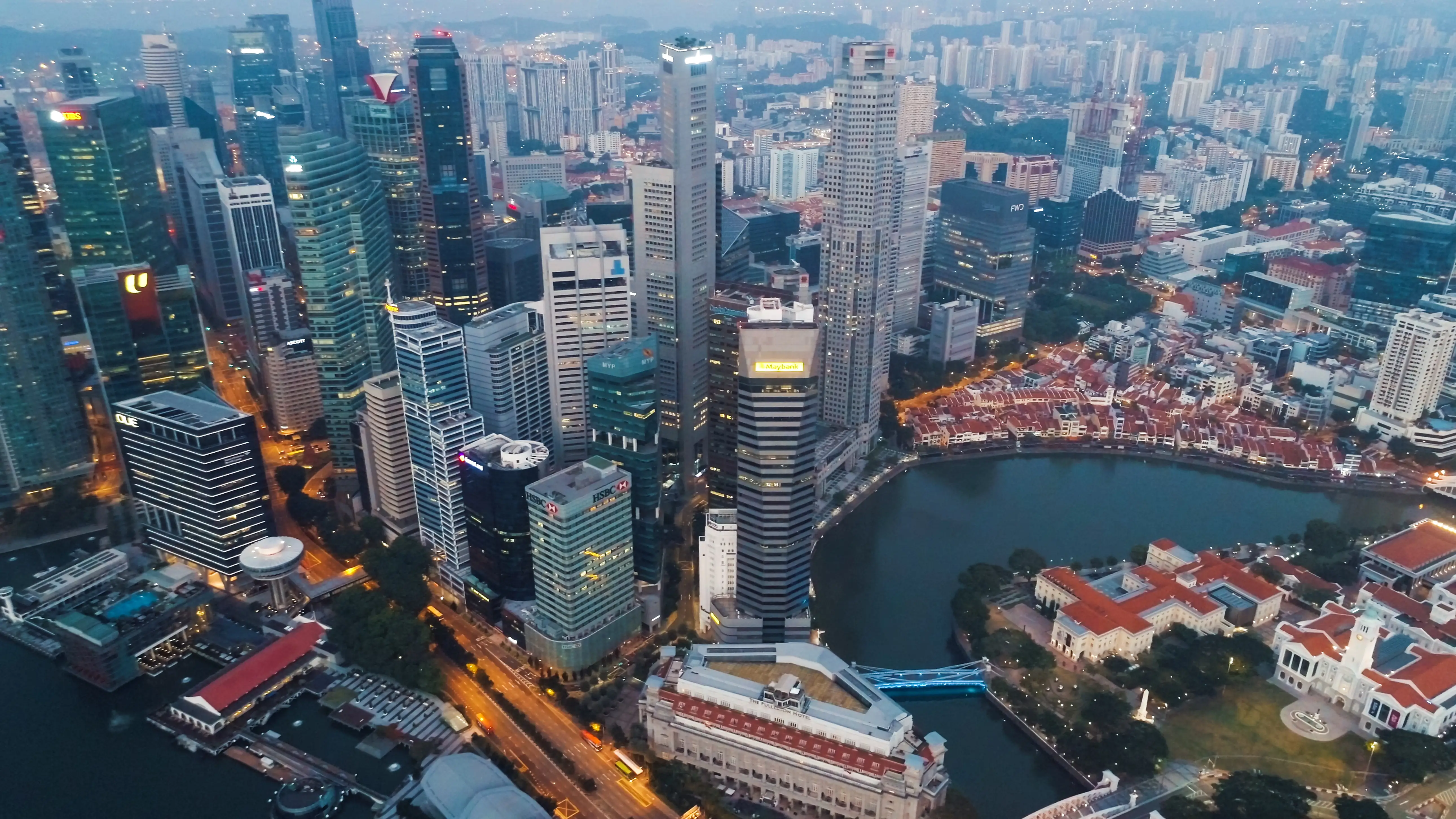 Aerial view of Singapore’s downtown skyline with skyscrapers, roads, and waterfront buildings around a bay at dusk.