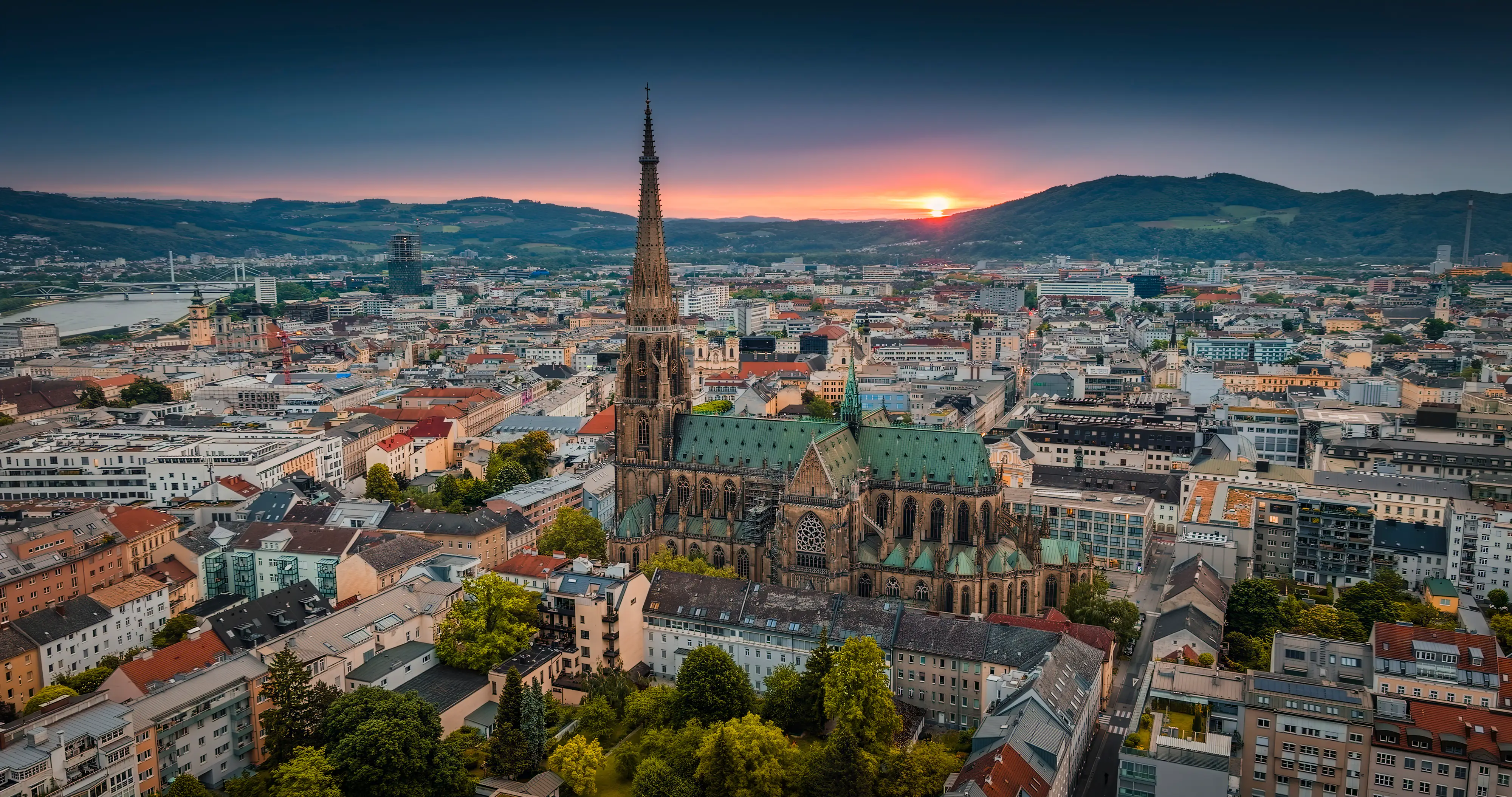 Aerial sunset view of Linz city center with the New Cathedral rising above surrounding streets and buildings.