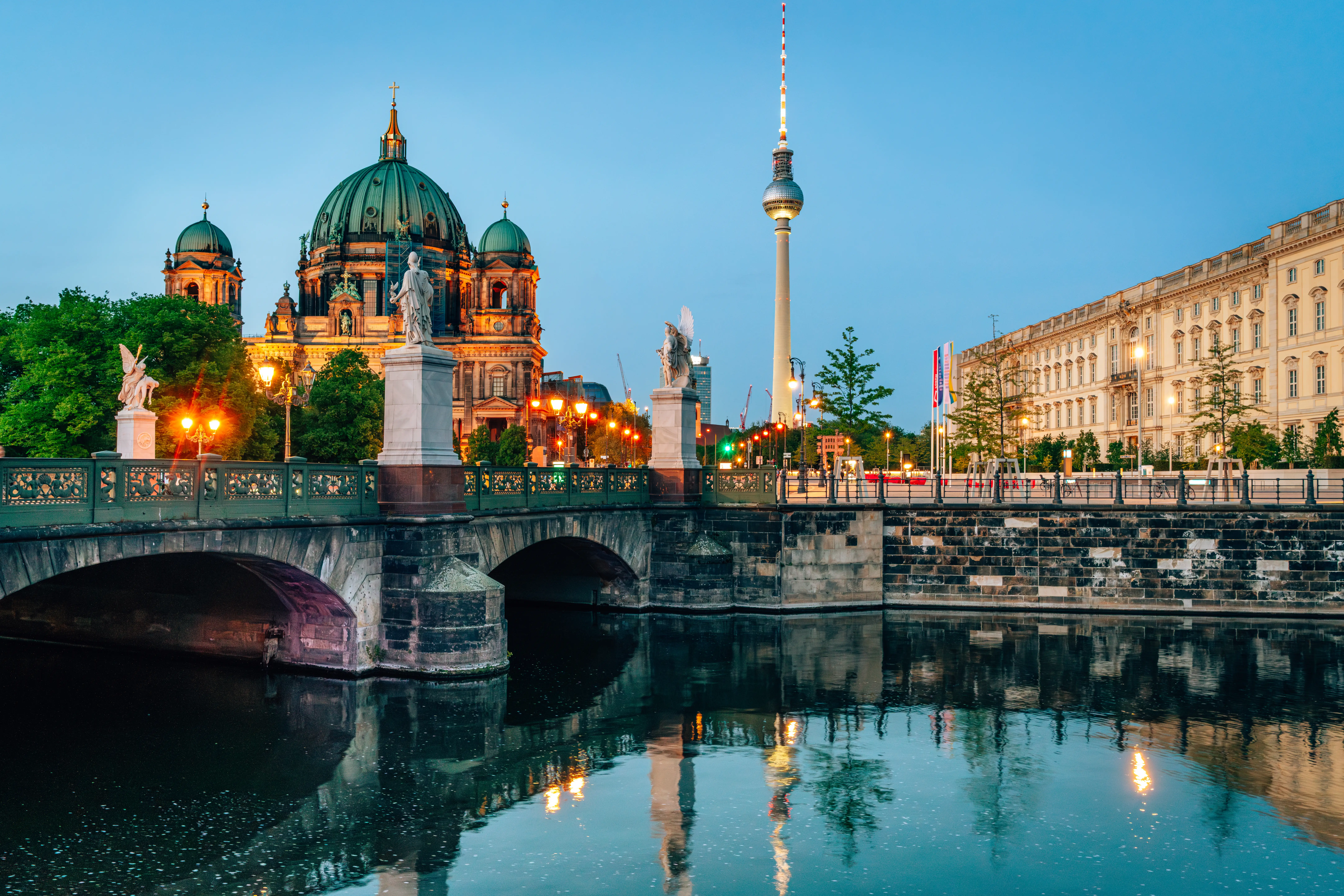 Berlin Cathedral and the Berlin TV Tower rise behind a bridge over the River Spree at dusk.