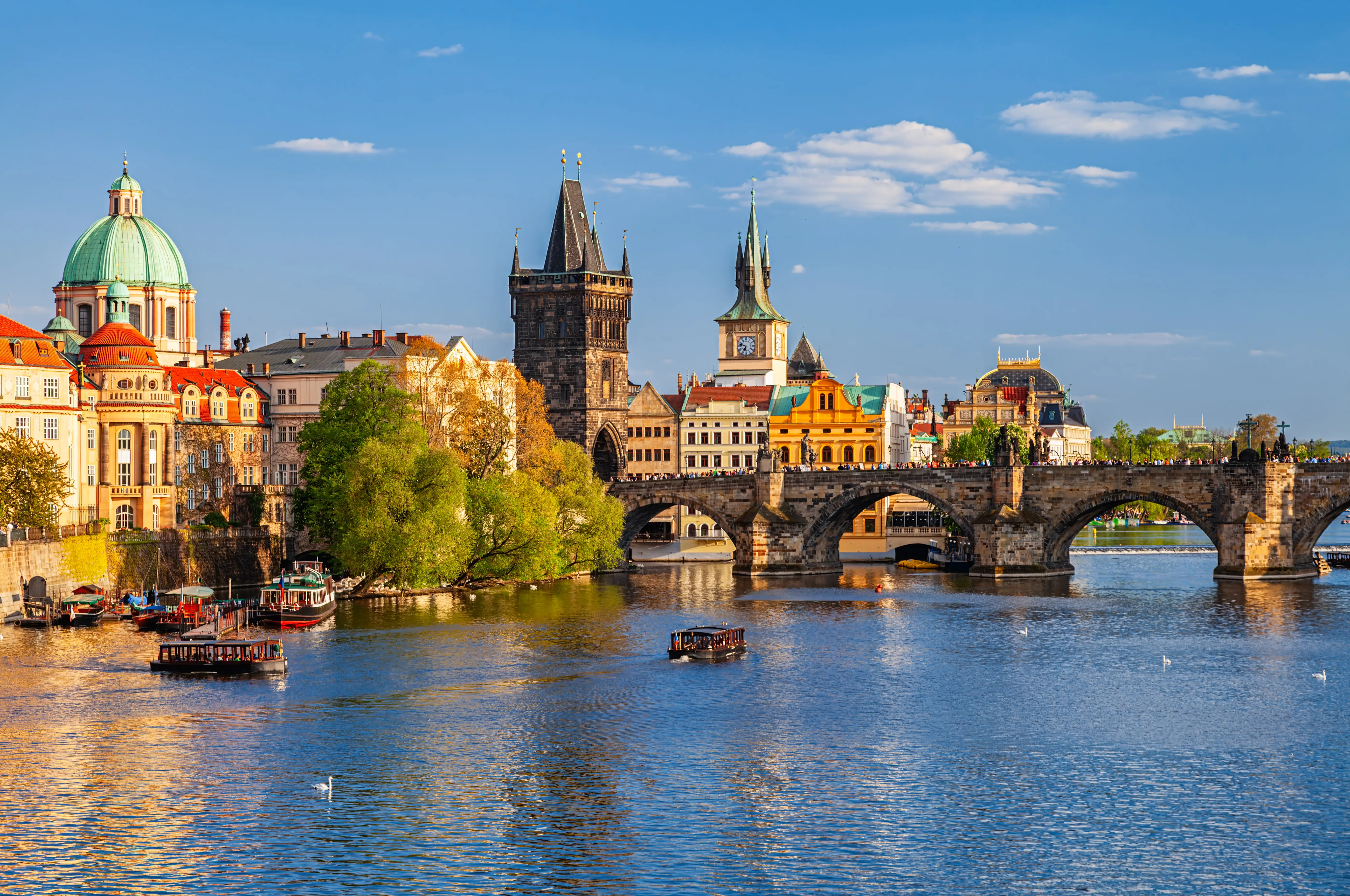 Charles Bridge spans the Vltava River with Prague’s historic Old Town skyline under a clear blue sky.
