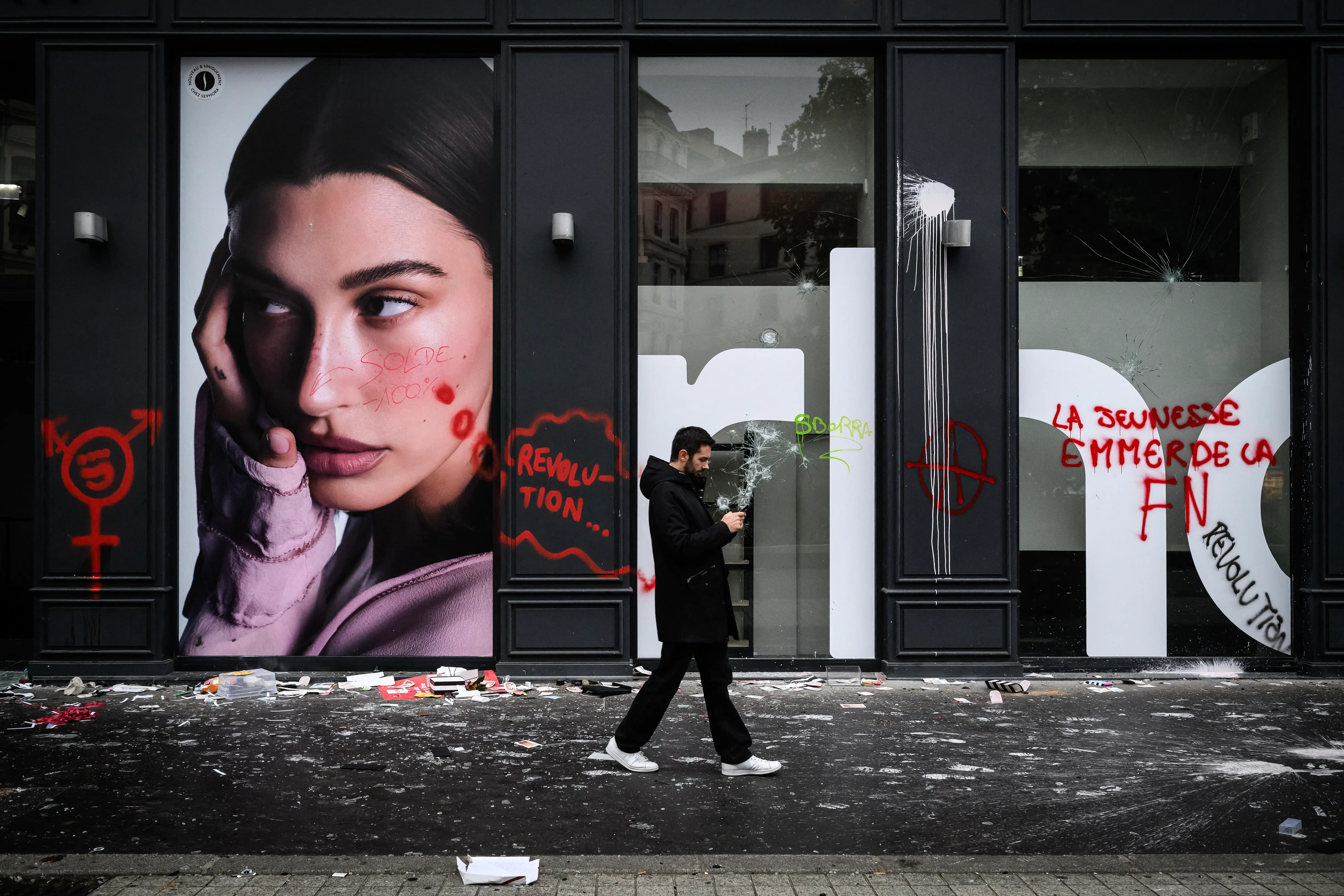 A pedestrian walks past a broken frontage windows of a shop and damages a day after riot and looting following a nationwide protest against the