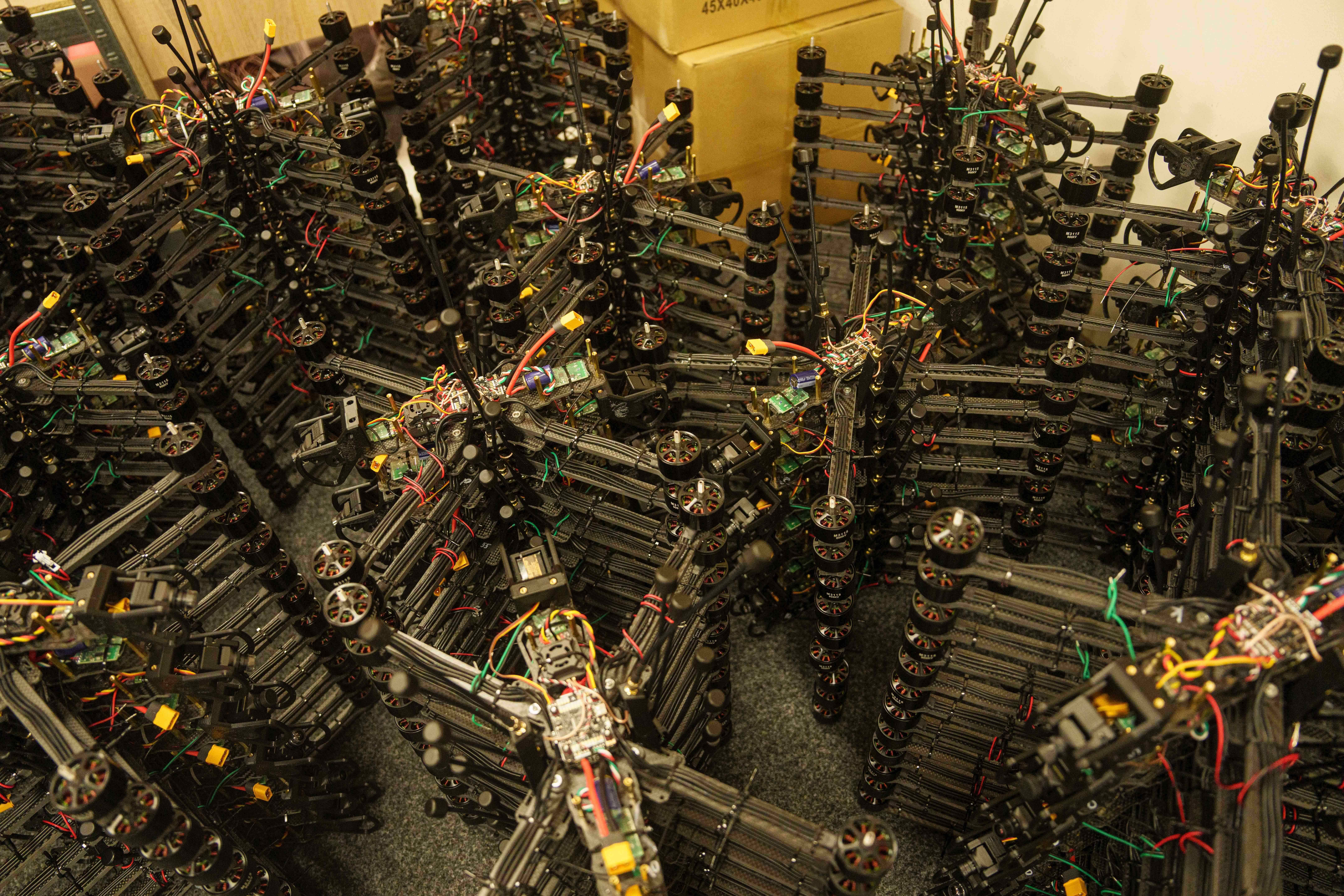 Stacks of partially assembled multirotor drones with exposed wiring and propeller motors fill an indoor workspace.